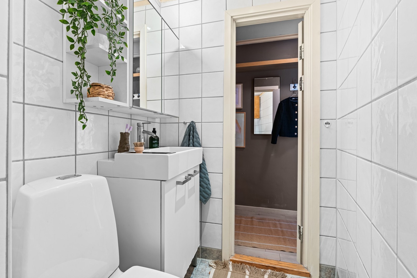 Baderomsinnredningen har glatte, folierte fronter og heldekkende servant, speilskap og lysarmatur på vegg over servanten, gulvmontert toalett og dusjhjørne med forheng Galleribilde