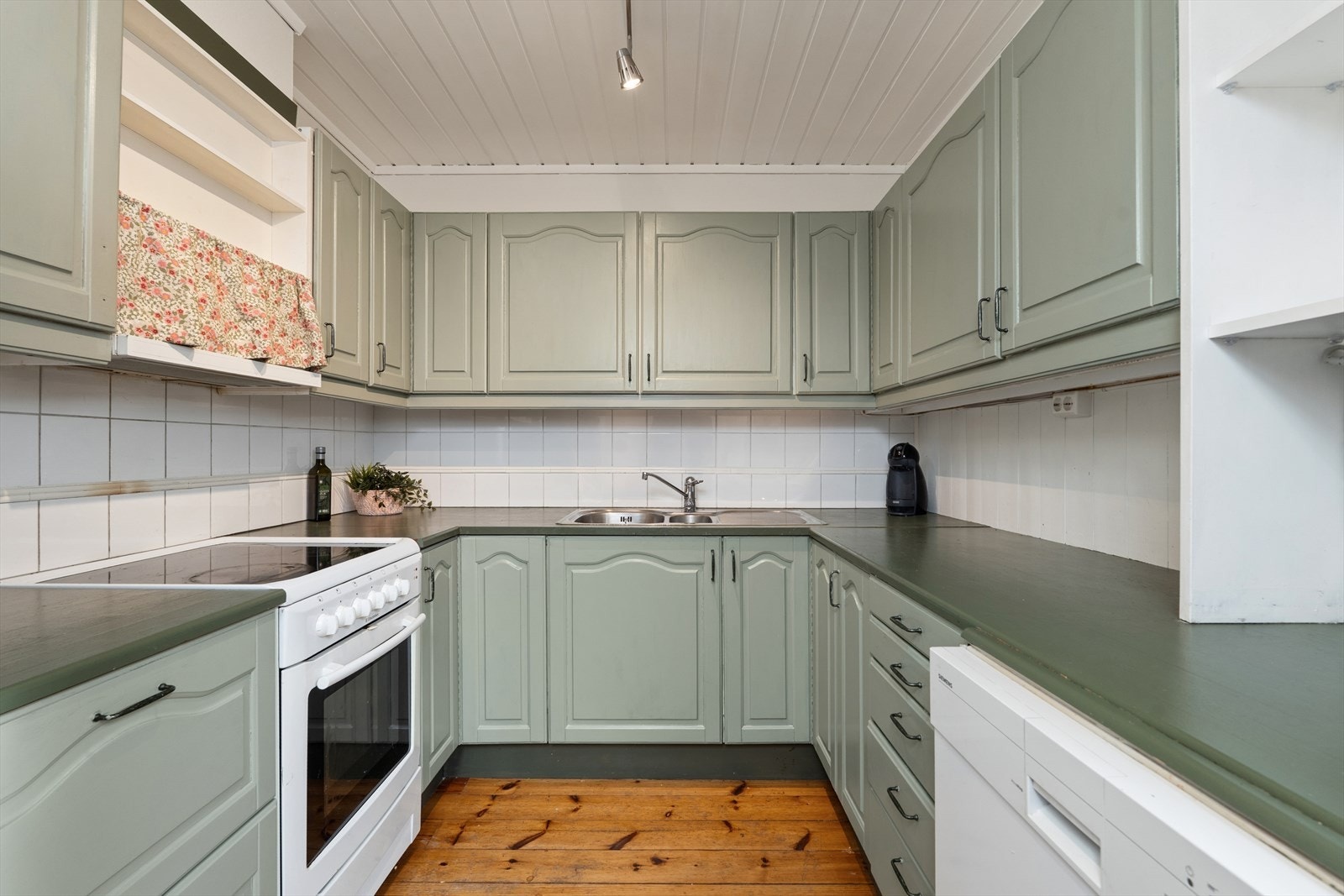 Kjøkkeninnredningen har profilerte fronter og en benkeplate i malt heltre. Det er keramiske fliser mellom over- og underskap. Galleribilde