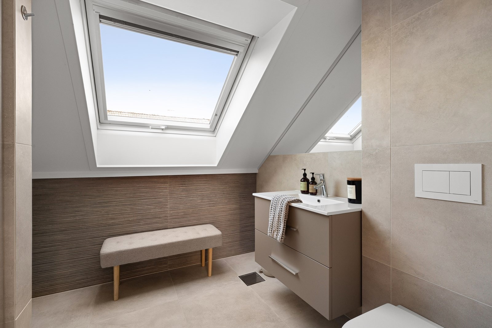Badet er moderne innredet med fliser på gulv og deler av vegger, varmekabler i gulv, samt servant, vegghengt toalett og dusjhjørne. Galleribilde