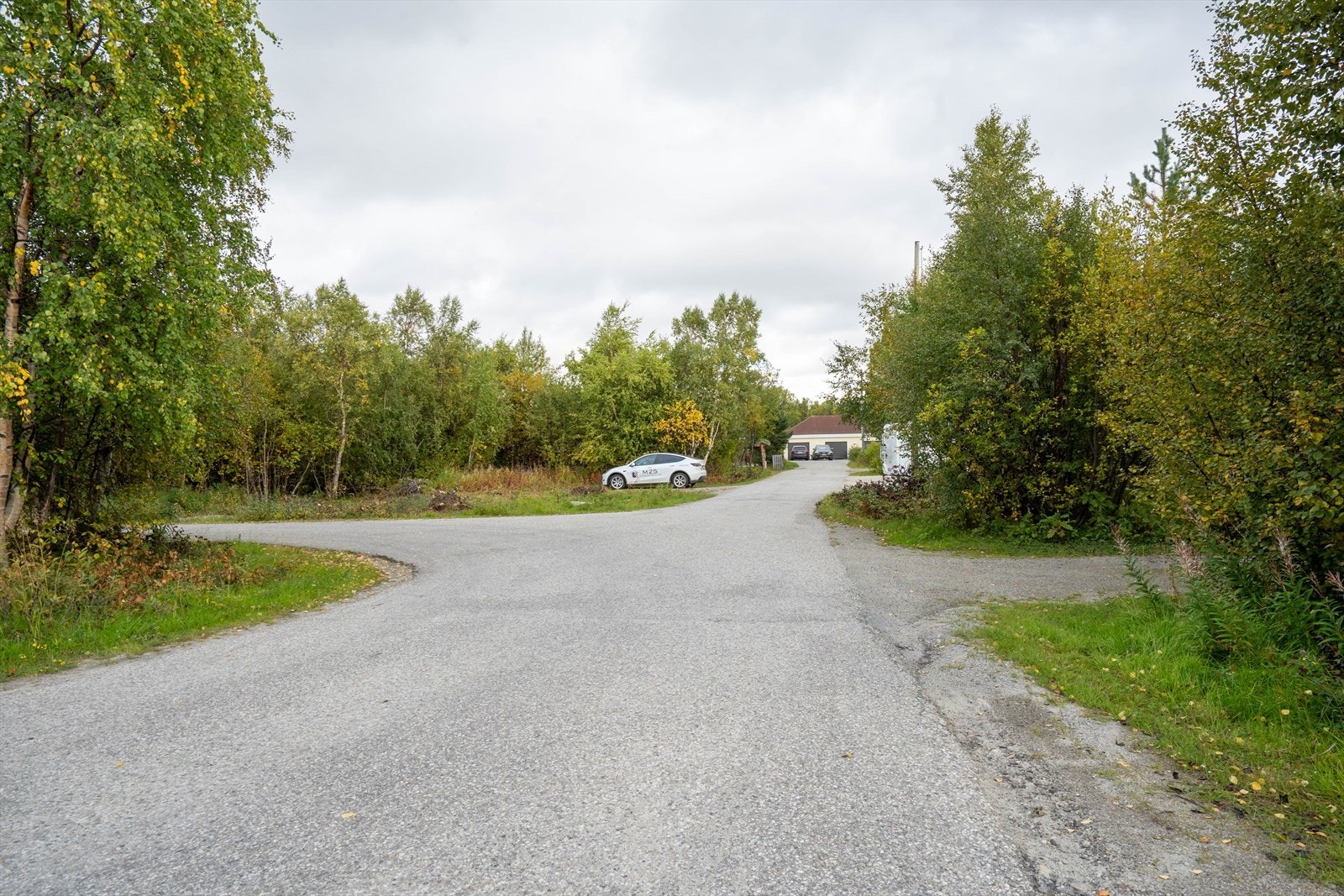 Tomten ligger til venstre i bildet hvor hvit bil står parkert, blindvei rett frem til eneboliger. Galleribilde