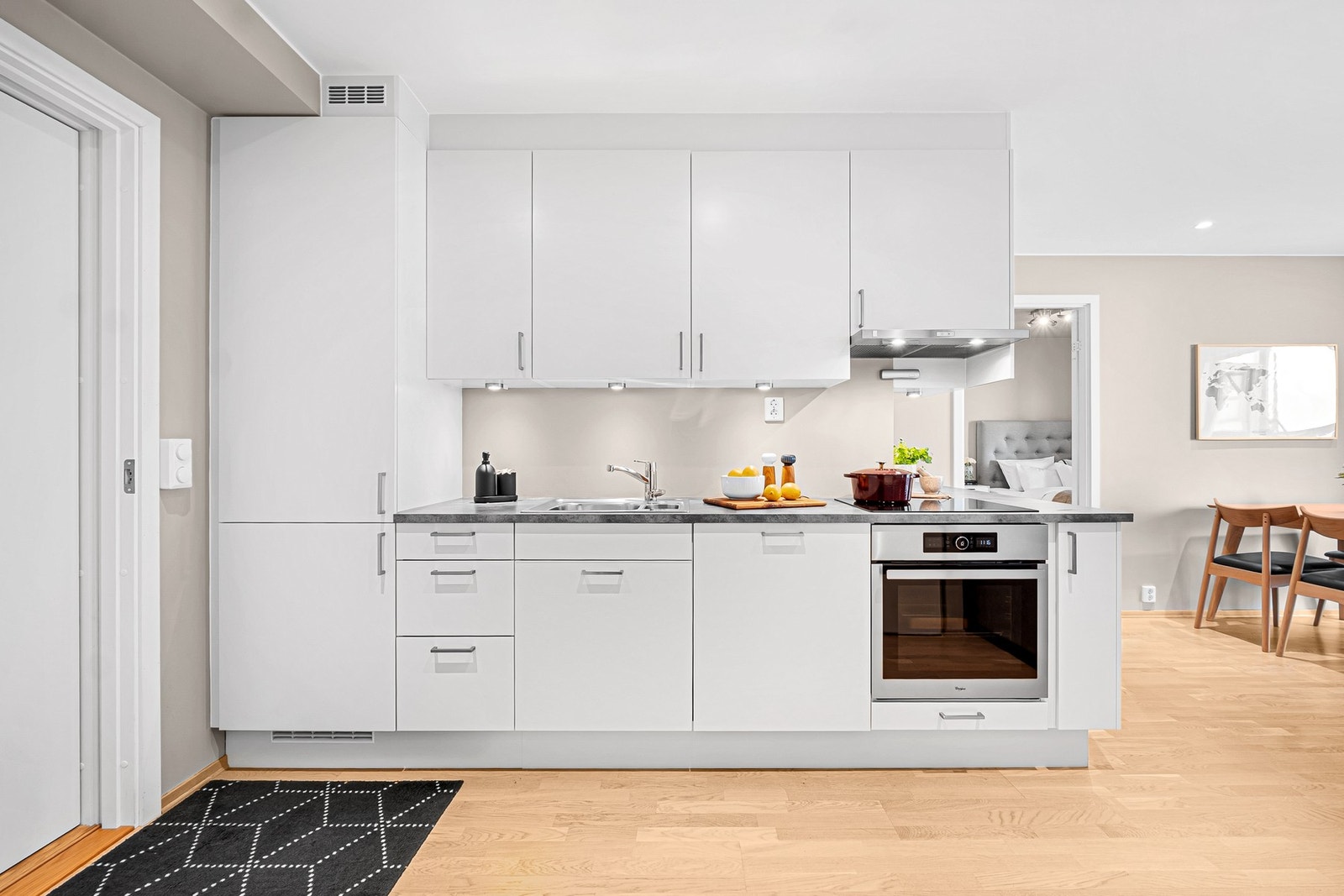 Lyst og moderne kjøkken med slette fronter og benkeplate i laminat. Integrerte hvitevarer som kjøl/frys, oppvaskmaskin, induksjonstopp og stekeovn. Galleribilde