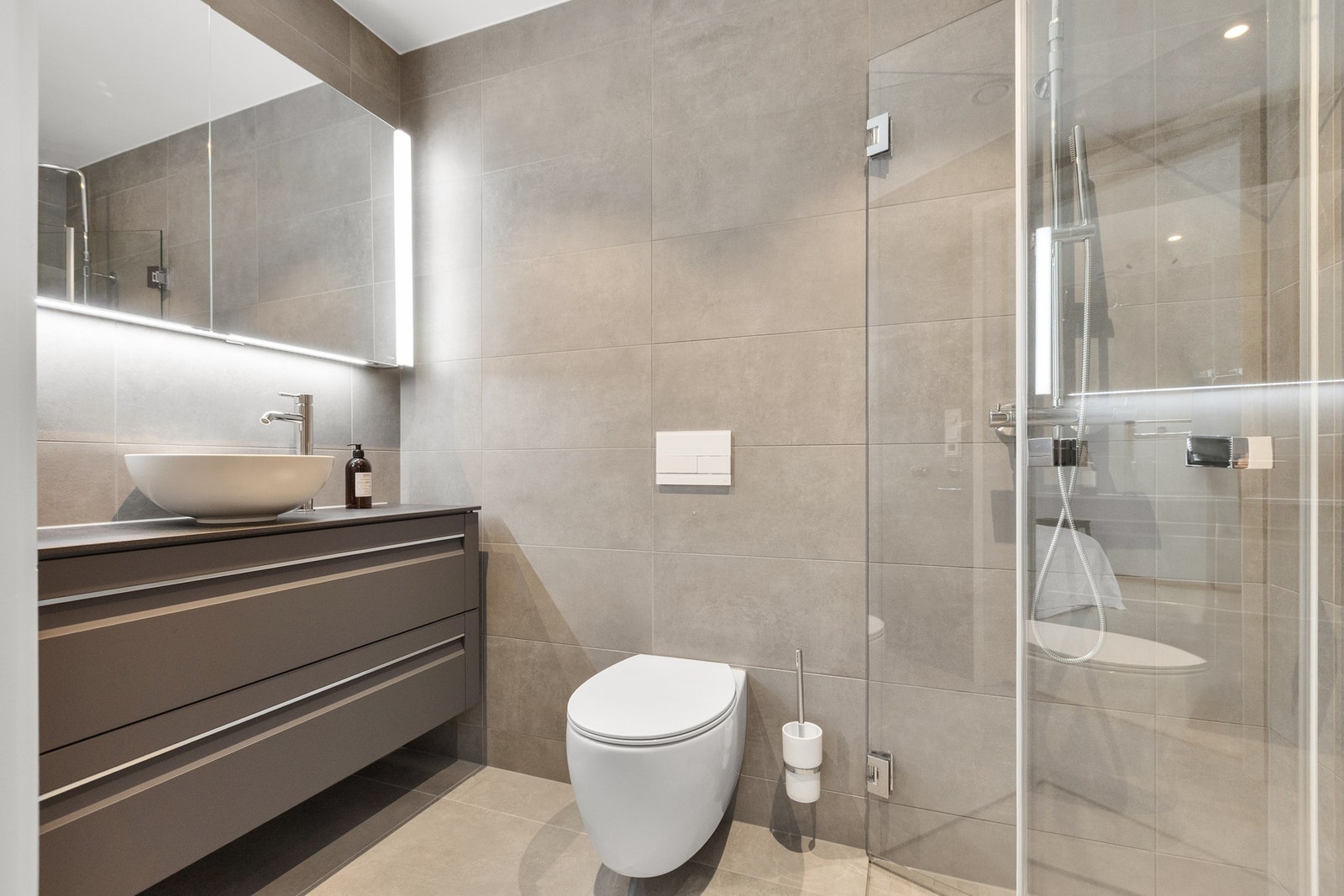 Videre inneholder etasjen et moderne bad med flislagte flater, gulvvarme, vegghengt toalett, stilren servantinnredning og dusjløsning Galleribilde