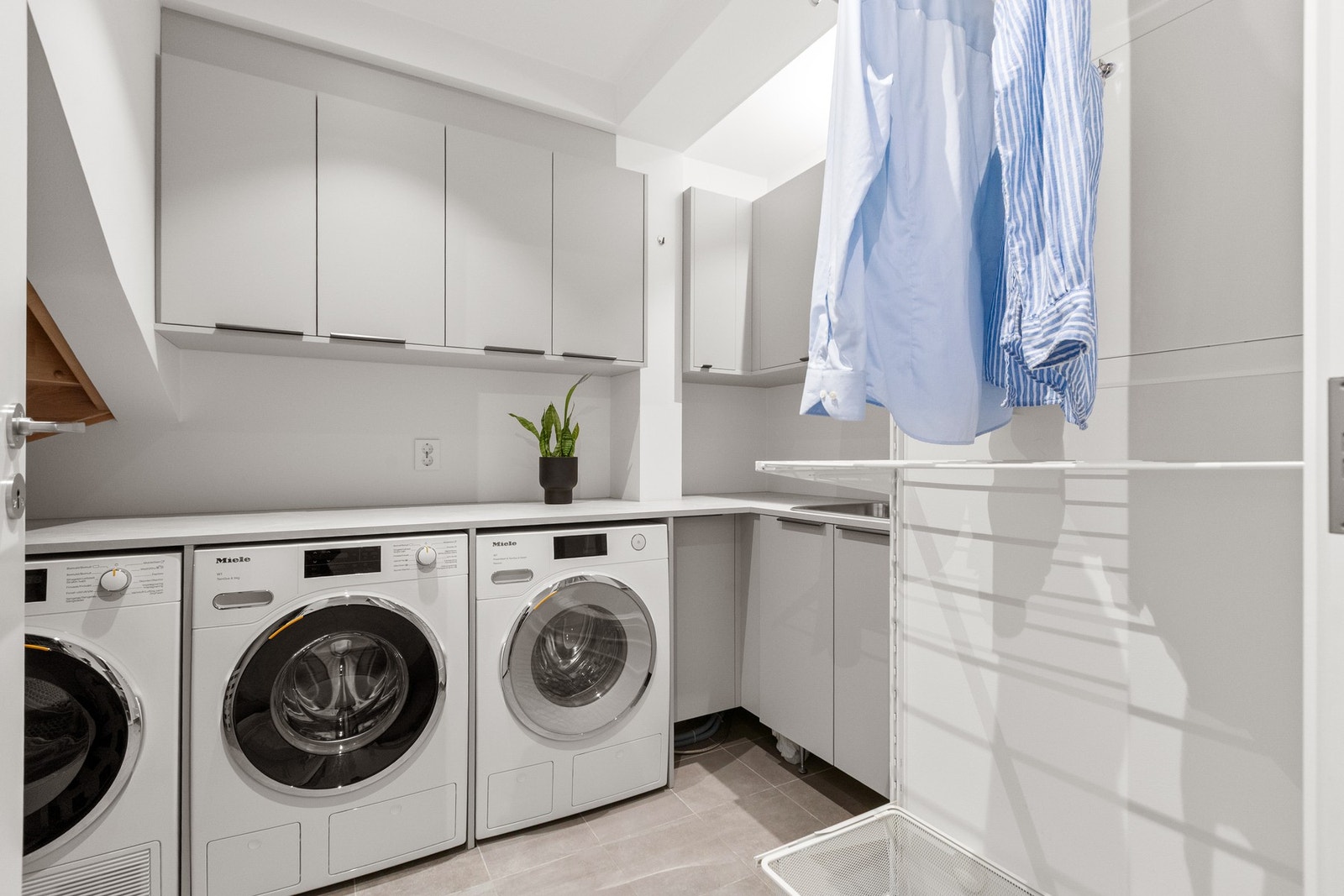 Vaskerommet er romslig og svært funksjonelt med flislagt gulv med varme, rikelig med skapplass, arbeidsbenk med nedfelt vaskekum og god tilrettelegging for flere vaskemaskiner og tørketromler. Galleribilde
