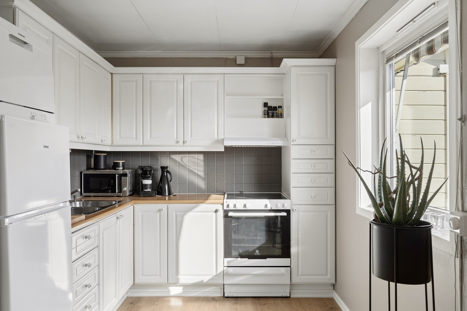 Lys profilert innredning, fliser over benk og gode arbeidsflater gir rommet en funksjonell og ryddig arbeidsstasjon. En naturlig samlingsplass i boligen med plass til både matlaging og sosialt samvær Galleribilde