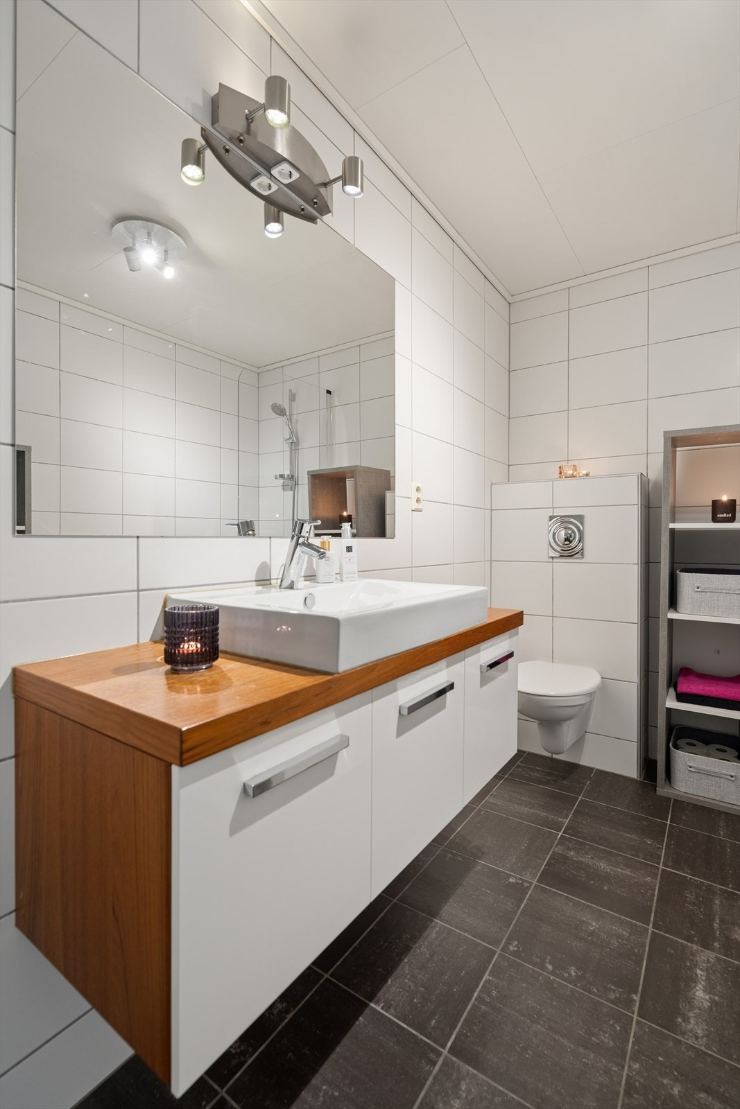 Rommet er innredet med en moderne baderomsseksjon med glatte fronter, benkeplate med overliggende servant og speil med integrert belysning. Videre er badet utstyrt med vegghengt toalett, badekar med glassvegg og dusjløsning, samt opplegg for vaskemaskin. Galleribilde