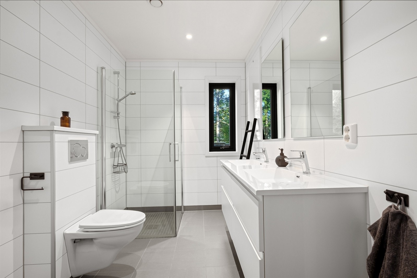 Badet har baderomsplater på vegger, flislagt gulv og downlights i himling. Innredningen består av toalett, dobbel servant med skuffeinnredning og speil. Dusjsonen har innfellbare glassdører og mosaikkfliser. Galleribilde