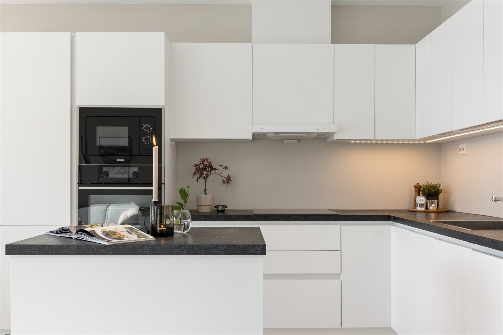 Stilrent kjøkken med hvite, slette fronter og mørk, laminert benkeplate. Galleribilde