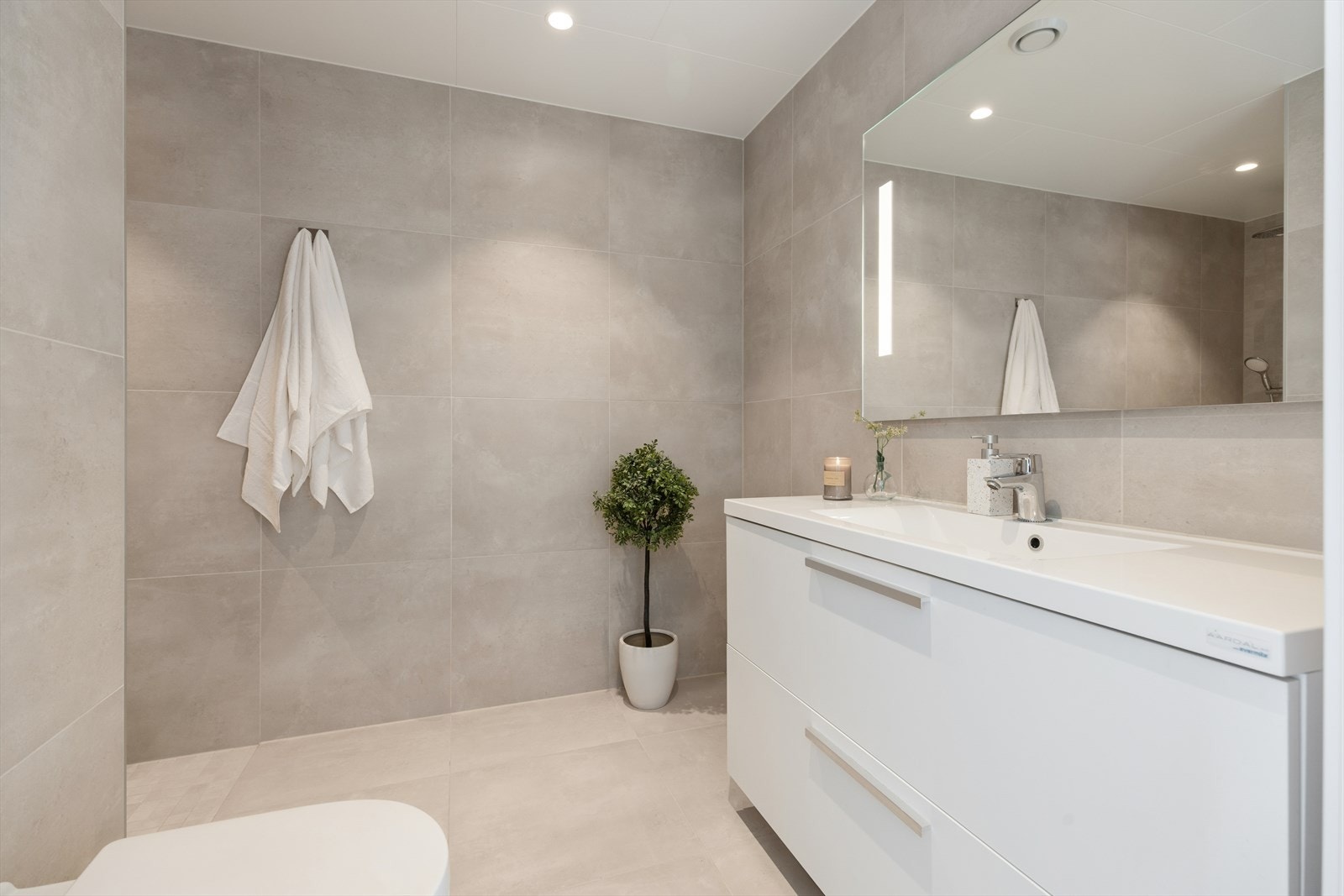 Lekkert flislagt bad i samme utførelse som 1. etasje. Utstyrt med servant med oppbevaing, åpen dusjløsning og vegghengt toalett. Galleribilde