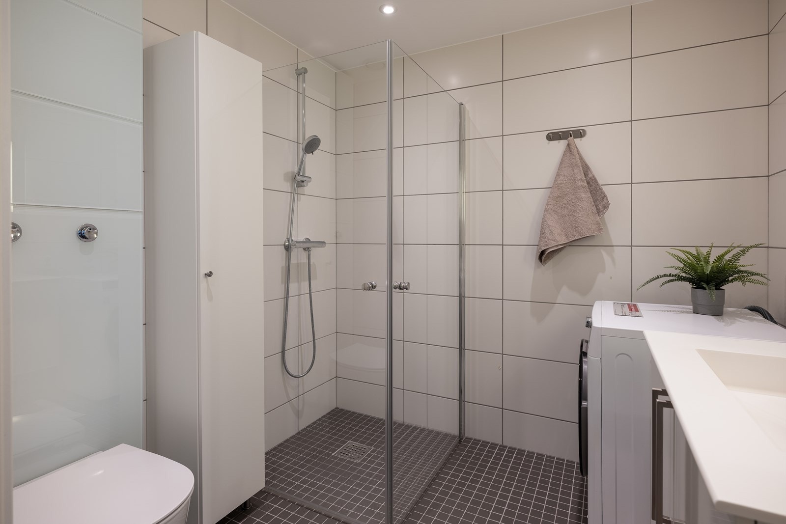 Badet byr på dusjhjørne, opplegg for vaskemaskin, servant, servantskap og veggmontert wc. Galleribilde