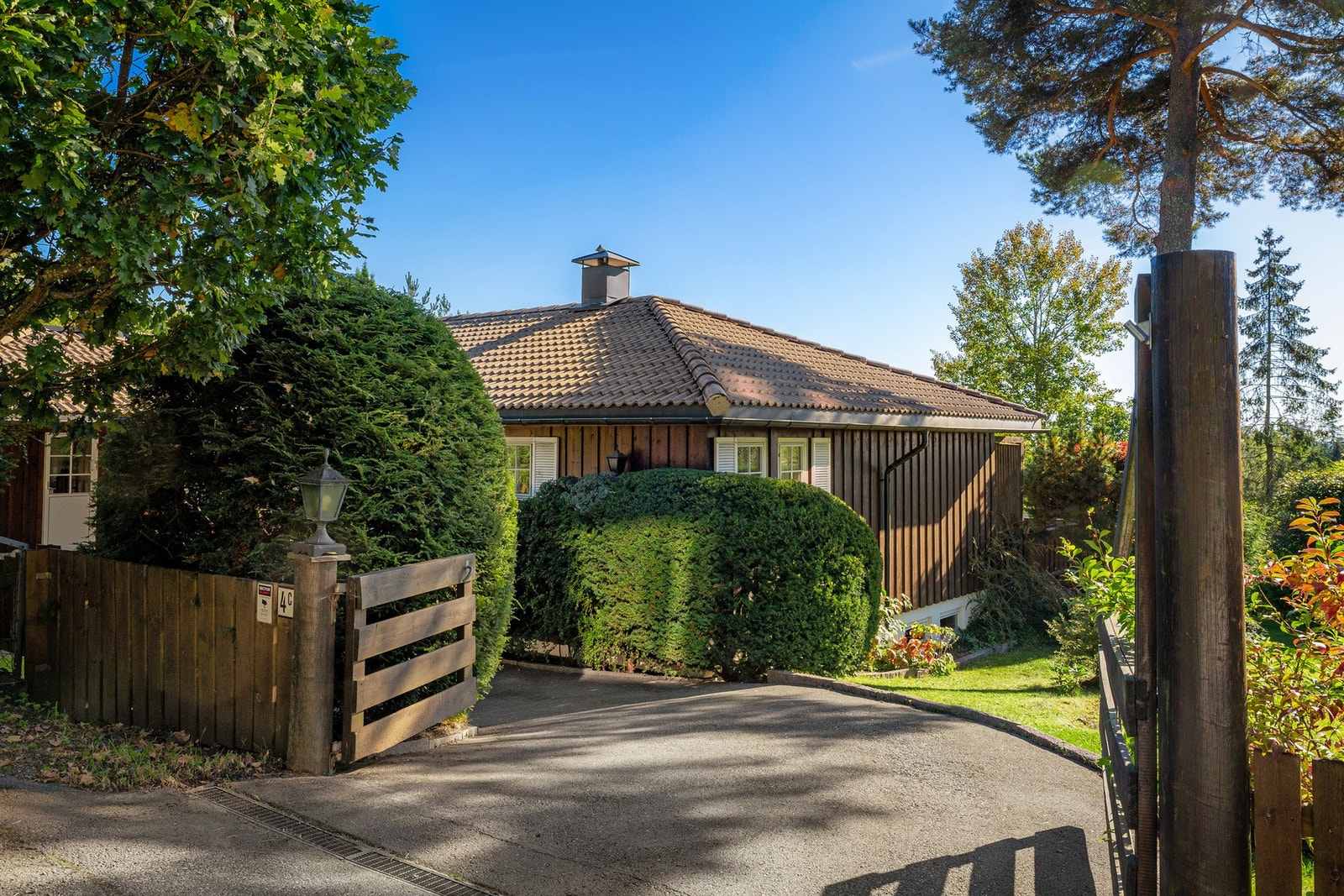 Innkjørsel med adkomst til eiendommen, rammet inn av port og frodig beplantning som gir et representativt førsteinntrykk. Galleribilde