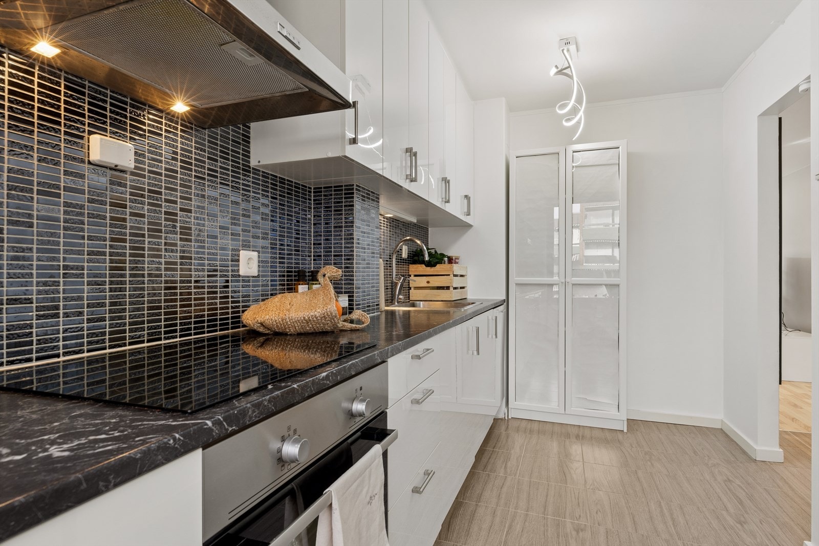 Innredningen har glatte, hvite fronter og laminatbenkeplate. Integrert induksjonstopp, stekeovn, oppvaskmaskin og kjøl/frys medfølger. Galleribilde