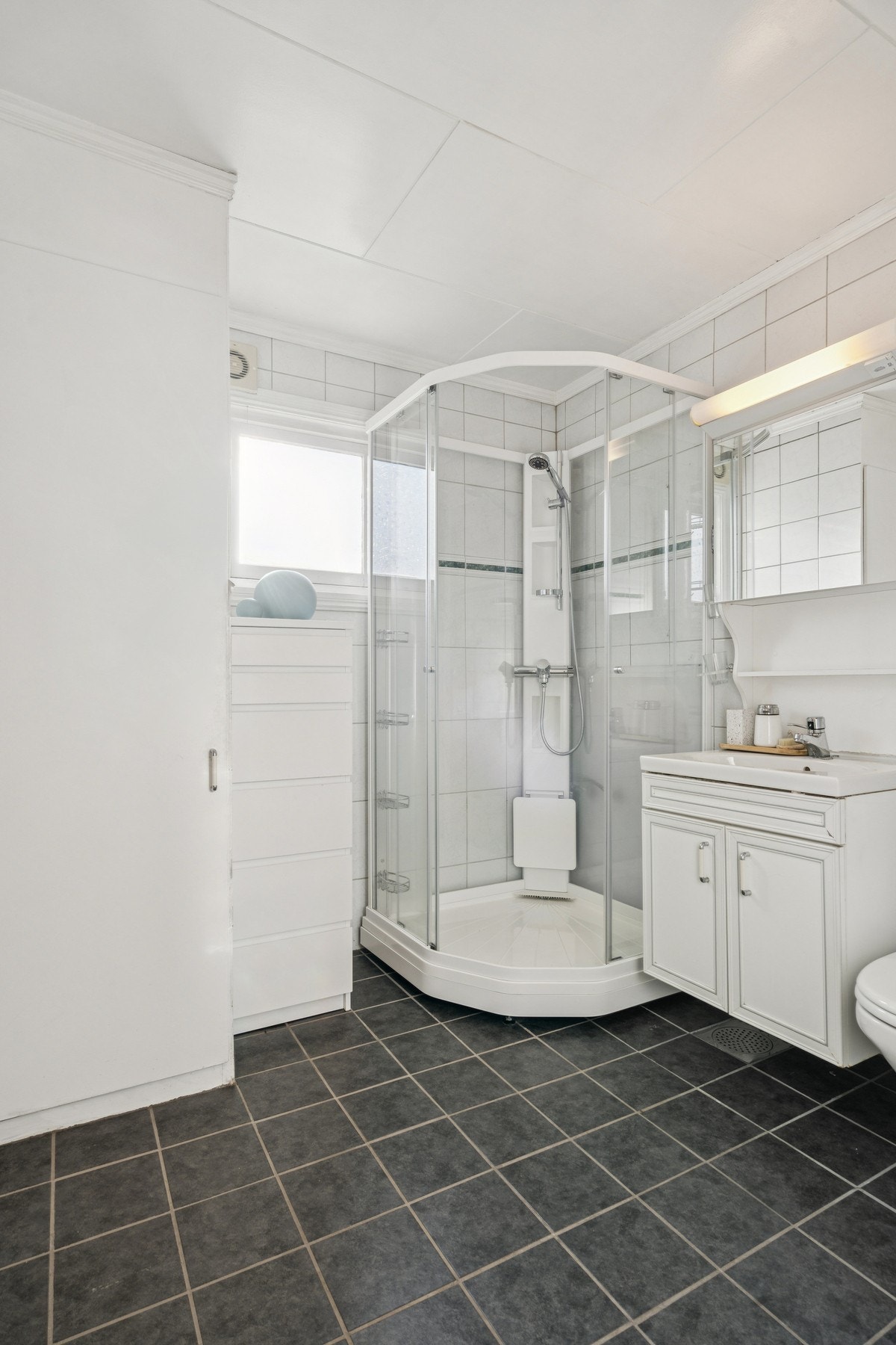 Badet i hovedetasjen har et dusjkabinett fra 2019 og et praktisk, plassbygget høyskap for oppbevaring. Galleribilde