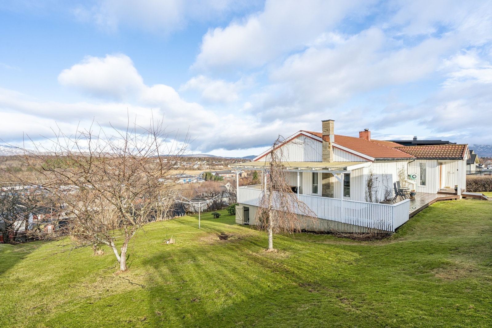 Eiendommen ligger i et skrånende terreng, opparbeidet med plen og prydbusker Galleribilde