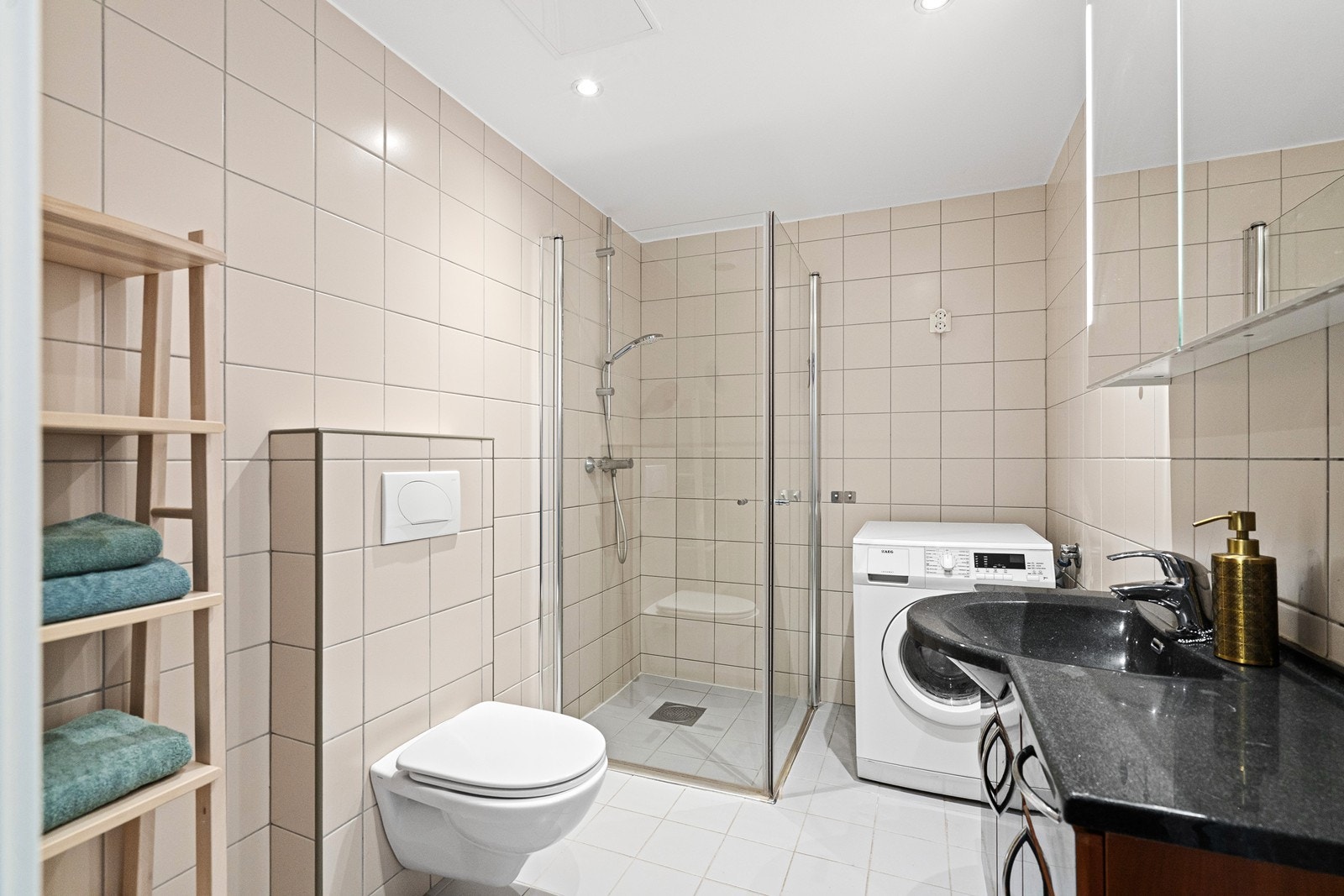 Flislagt bad med behagelig gulvvarme. Baderommet er innredet med servant i seksjon med speil og overlys, god oppbevaring i skuffer og skap, vegghengt toalett og et praktisk dusjhjørne med foldbare glassdører som gir en luftig romfølelse. Galleribilde