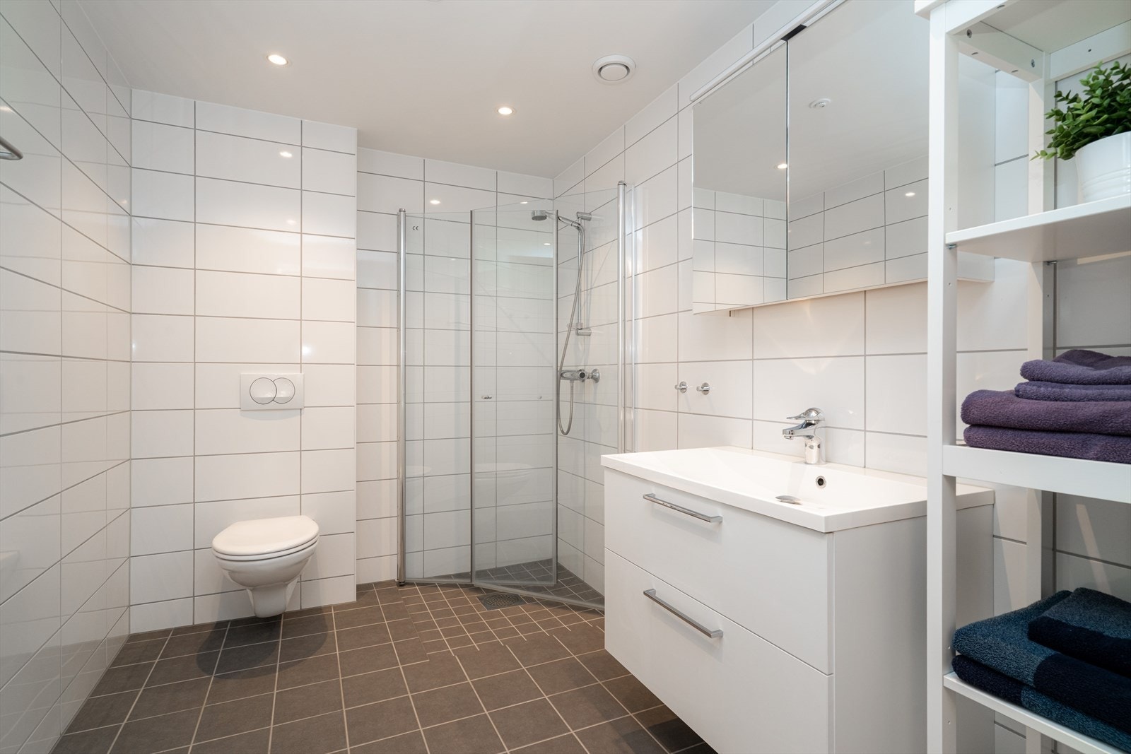 Moderne bad med fliser på gulv og vegger, og elektriske varmekabler som gir behagelig varme. Badet har romslig baderomsmøblement med god skuffplass, nedfelt servant og stor speilflate med tilhørende belysning Galleribilde