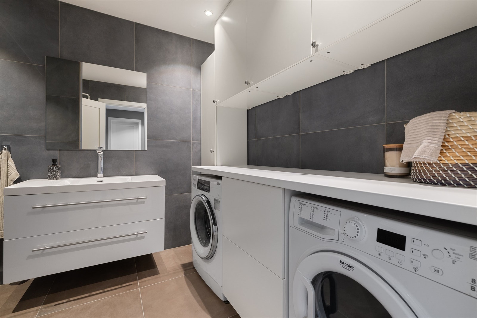 Flislagt vaskerom med mye lagringsplass og praktisk brettebenk Galleribilde