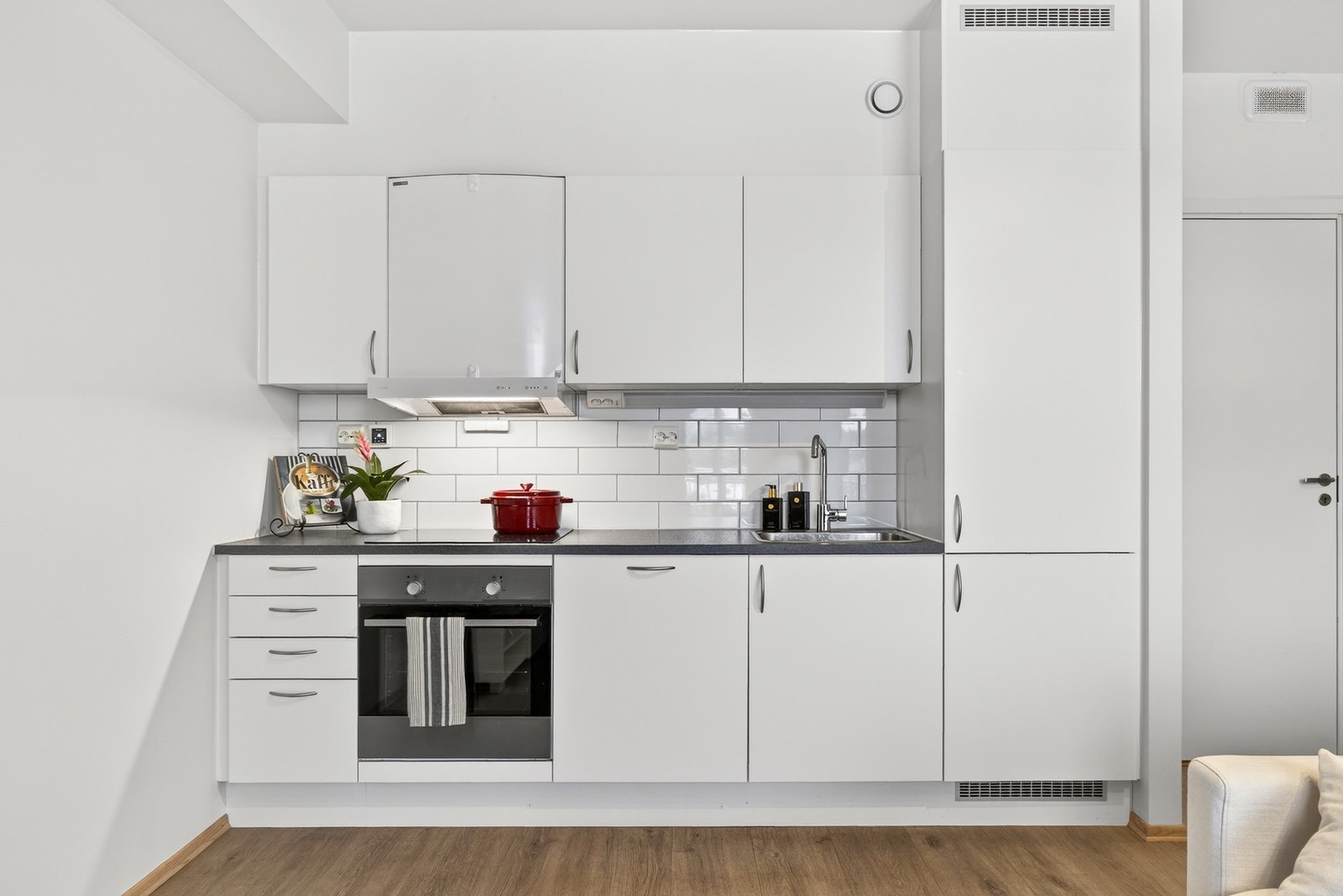 Moderne kjøkken i åpen løsning mot stuen, med slette fronter, belysning under overskap og fliser over benkeskap. Galleribilde