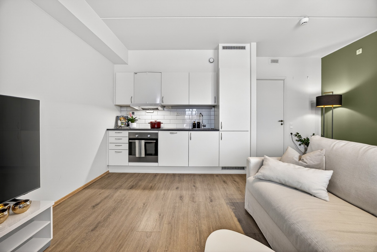 Den åpne stuen fremstår som meget innbydende med parkett på gulv, lysmalte slette veggflater, samt en grønnmalt fondvegg. Galleribilde