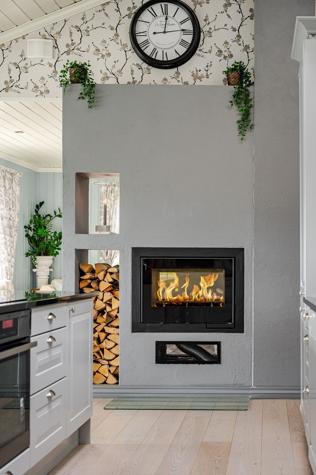 Som et fint midtpunkt i rommet er det en lekker peis som både gir god varme og bidrar til ekstra hygge. Flott gjennomgående innsats med dør på begge sider. Åpne hyller for oppbevaring av ved. Galleribilde