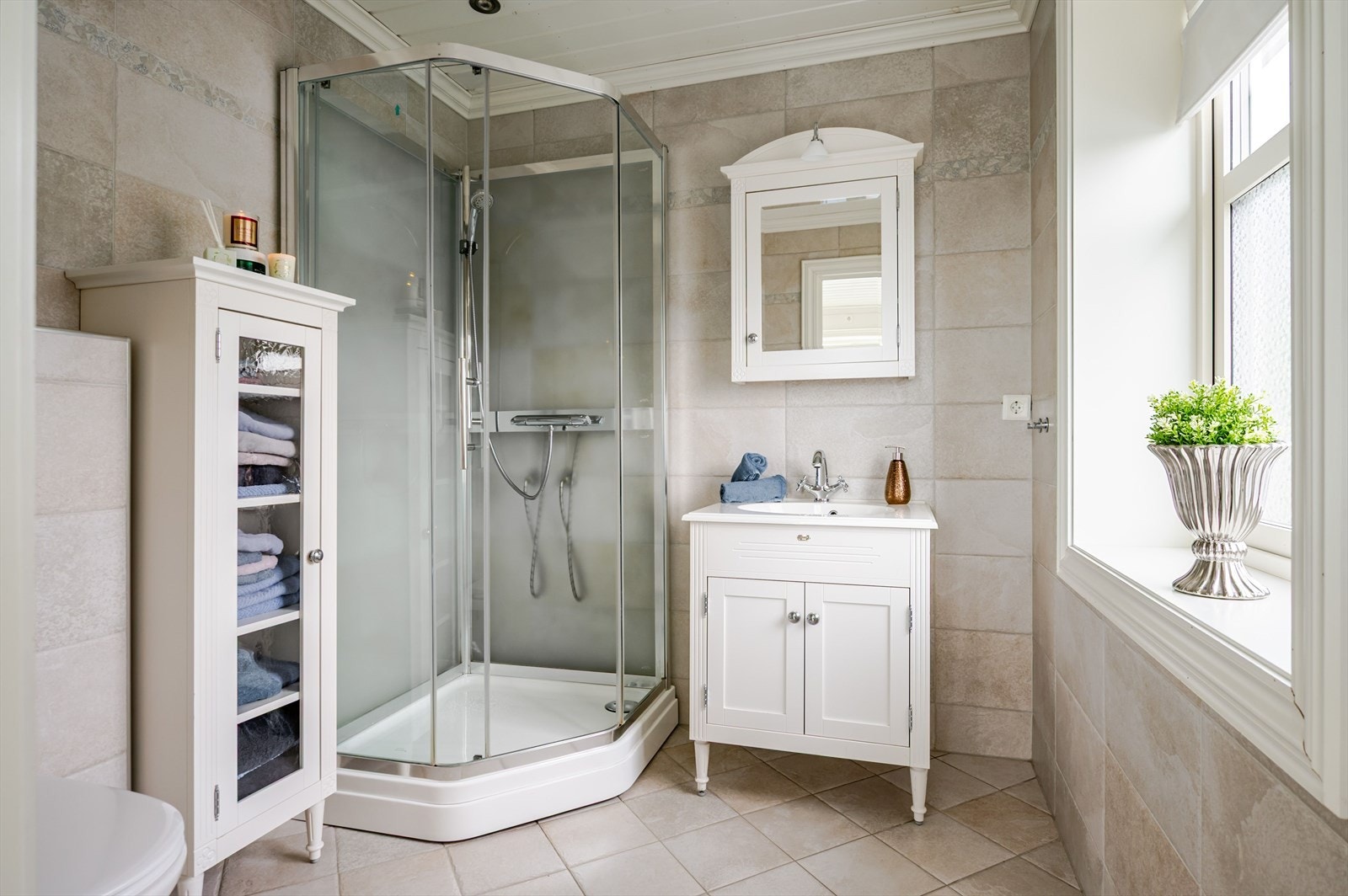 Lyst og pent baderom fra 2015 med adkomst fra hovedsoverommet. Baderommet har flotte fliser på gulv og vegger, elektriske varmekabler, downlights i himlingen, balansert ventilasjon og et stort vindu som slipper inn deilig dagslys. Galleribilde