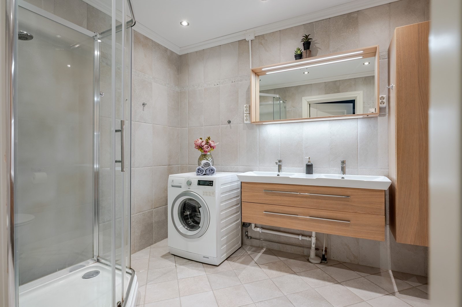 Lyst og innbydende bad/vaskerom fra 2015 i hybeldelen. Baderommet har delikate fliser på gulv og vegger, elektriske varmekabler, downlights i himlingen og balansert ventilasjon. Pen innredning med dobbel servant. Galleribilde