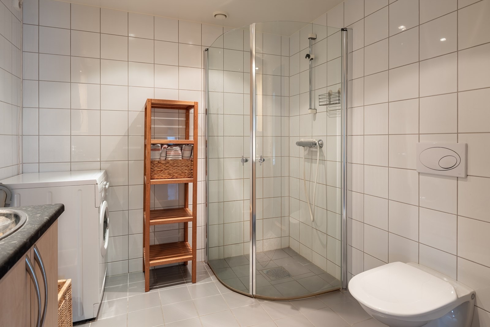 Videre er badet utstyrt med dusjhjørne, rørskap i tak, opplegg for vaskemaskin og servant i servantskap. Galleribilde