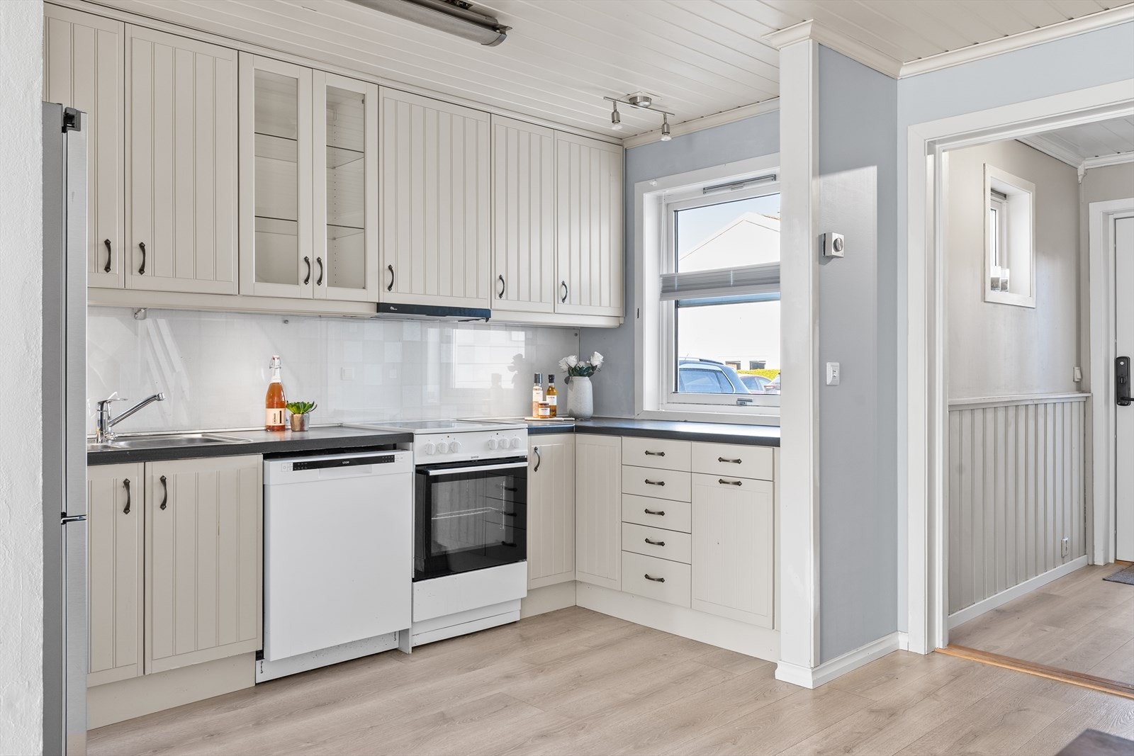 Med samme harmoniske farger som resten av boligen gir kjøkkenet en elegant overgang til stuen, utstyrt med profilerte fronter og laminatbenkeplate. Galleribilde