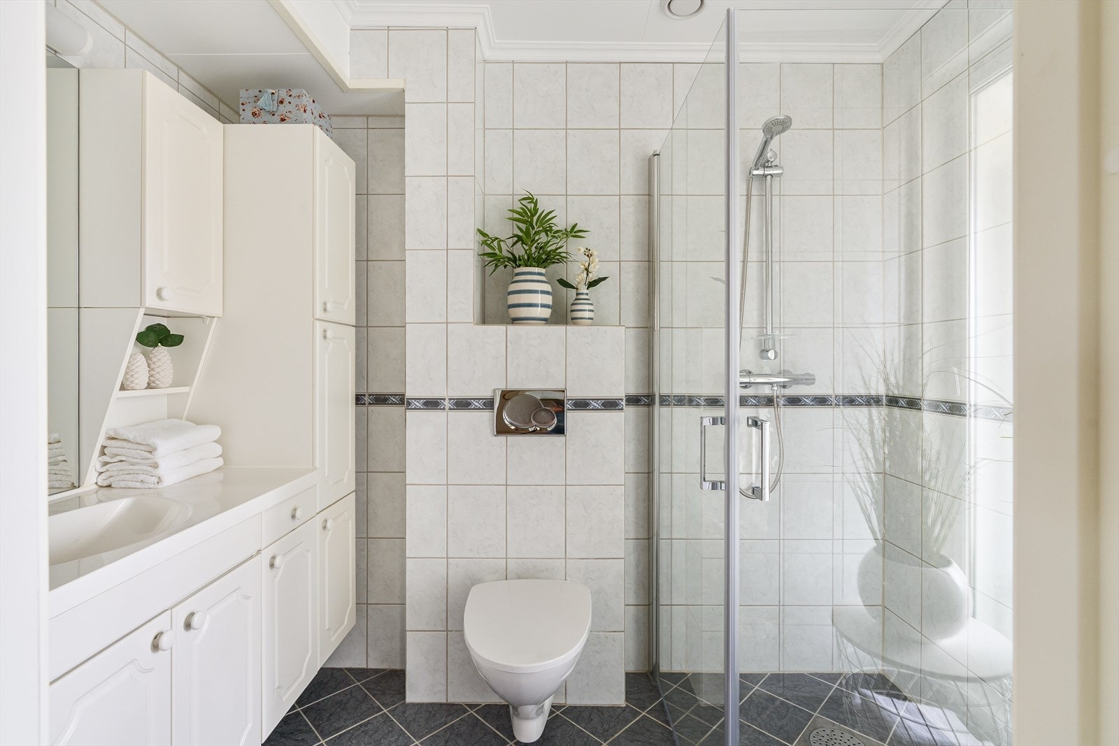 Helflist baderom med vask i seksjon med skap. Dusjhjørne og vegghengt toalett. Galleribilde