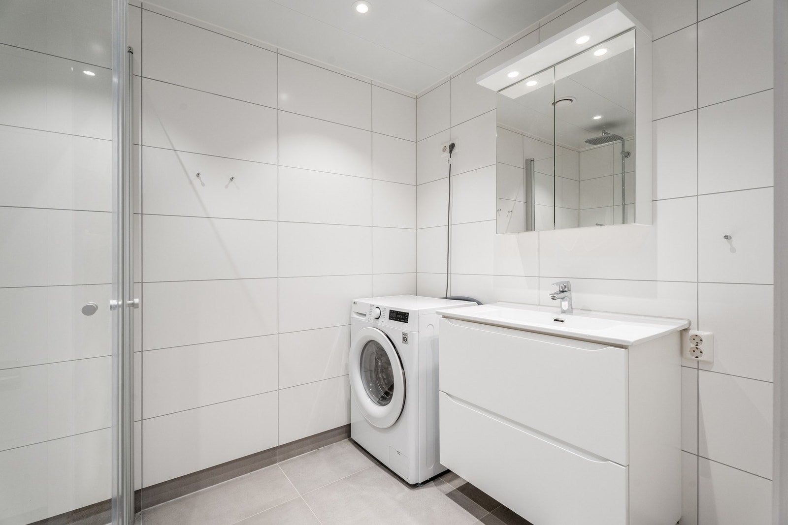 Flott baderom med 30x60-fliser på vegg og 60x60-fliser på gulv, elektrisk gulvvarme og opplegg for vaskemaskin. Galleribilde