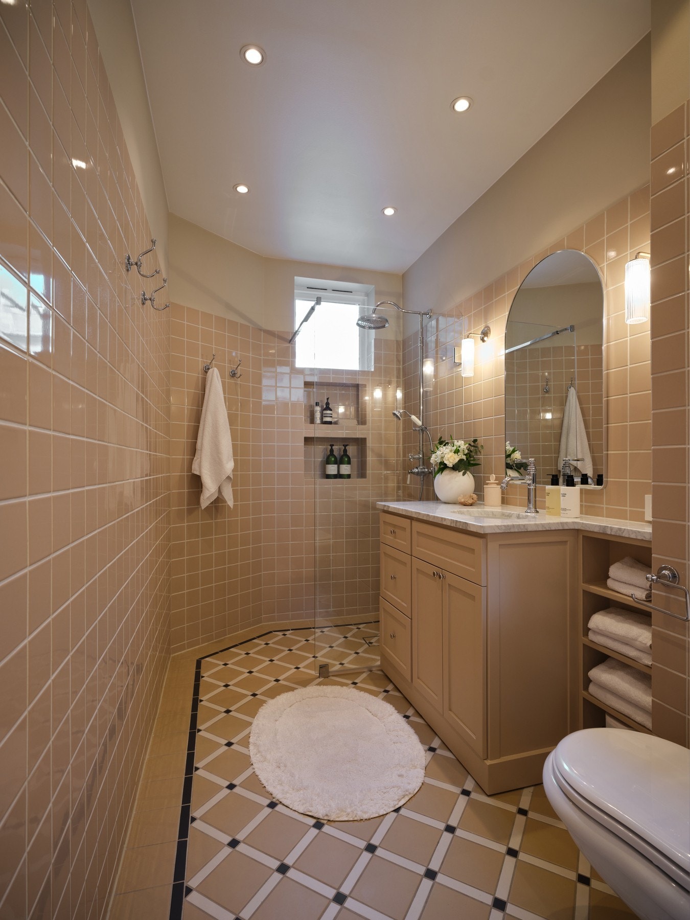 Delikat og gjennomført bad fra 2025 med et stilrent, klassisk uttrykk. Flislagte overflater i varme toner på både vegger og gulv gir en lun atmosfære, samtidig som innfelte downlights i himling sørger for god og jevn belysning. Galleribilde