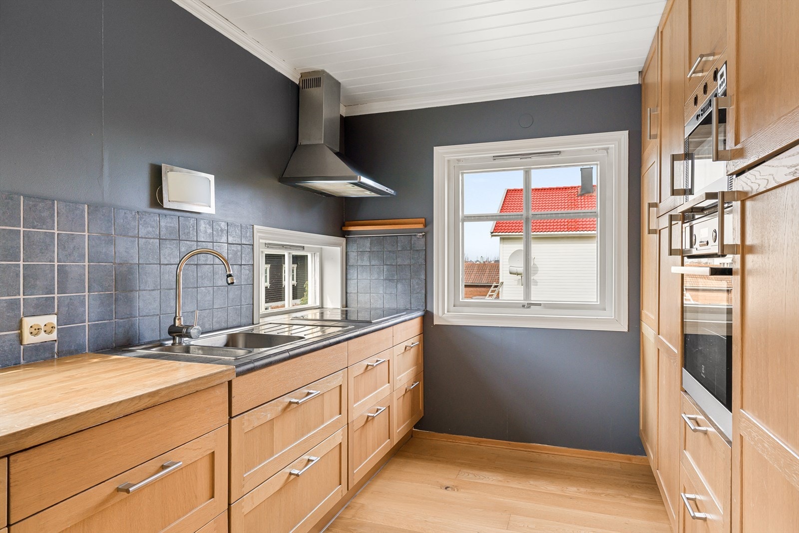 Her finner du takhøy innredning, heltre benkeplate, integrerte hvitevarer og stilfulle, mørke fliser over benken. Galleribilde