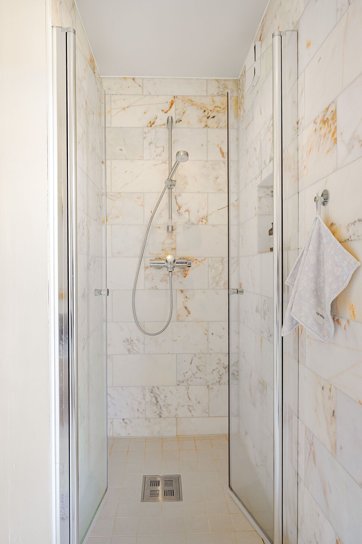 Dusjsonen har mindre fliser i samme fargetoner på gulv og marmorfliser på vegg som tilfører dybde og karakter. En integrert nisje i dusjen gir praktisk oppbevaring. Galleribilde