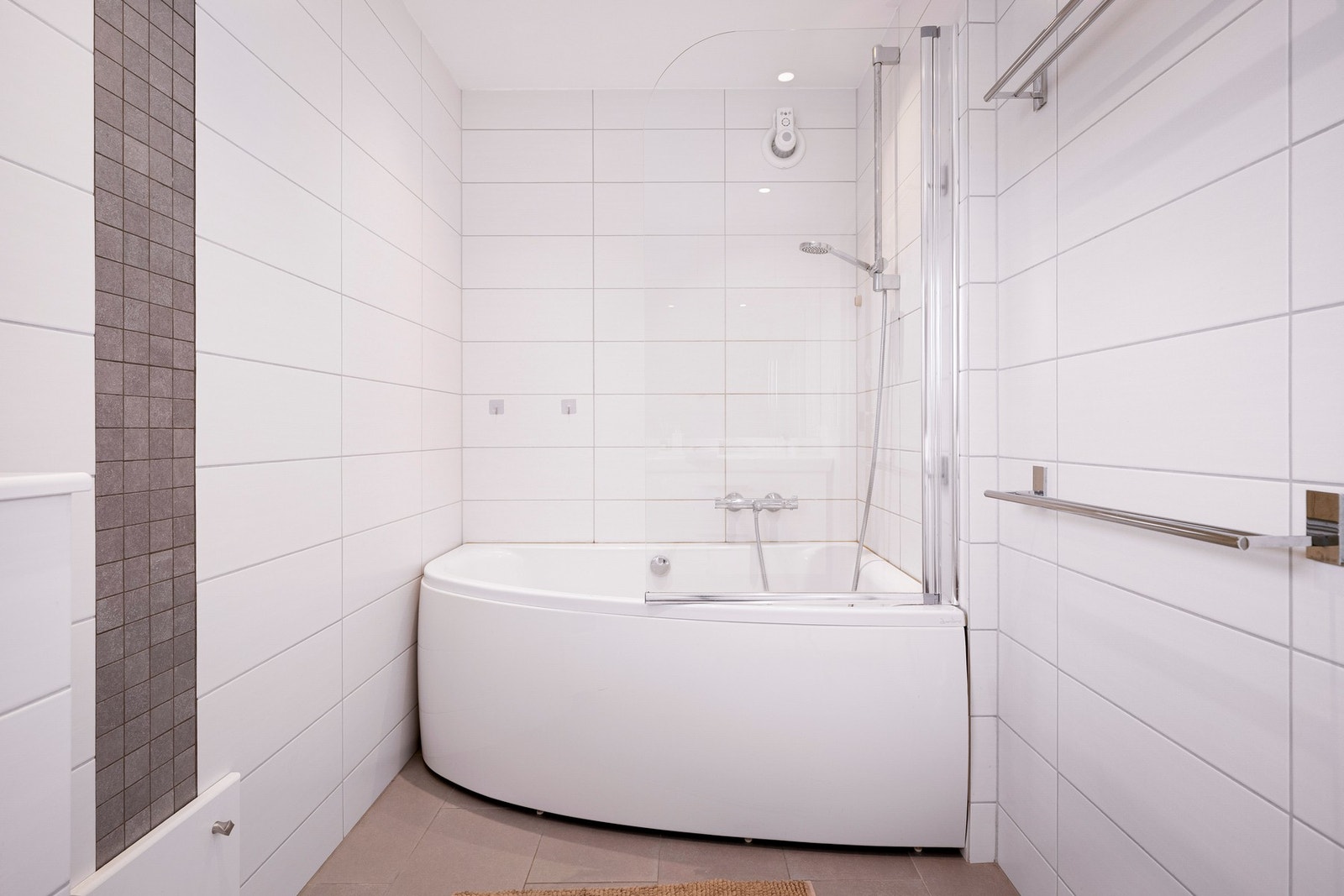 Badet er innredet med badekar med glassvegg, vegghengt toalett og baderomsinnredning med servant og oppbevaringsplass. Galleribilde