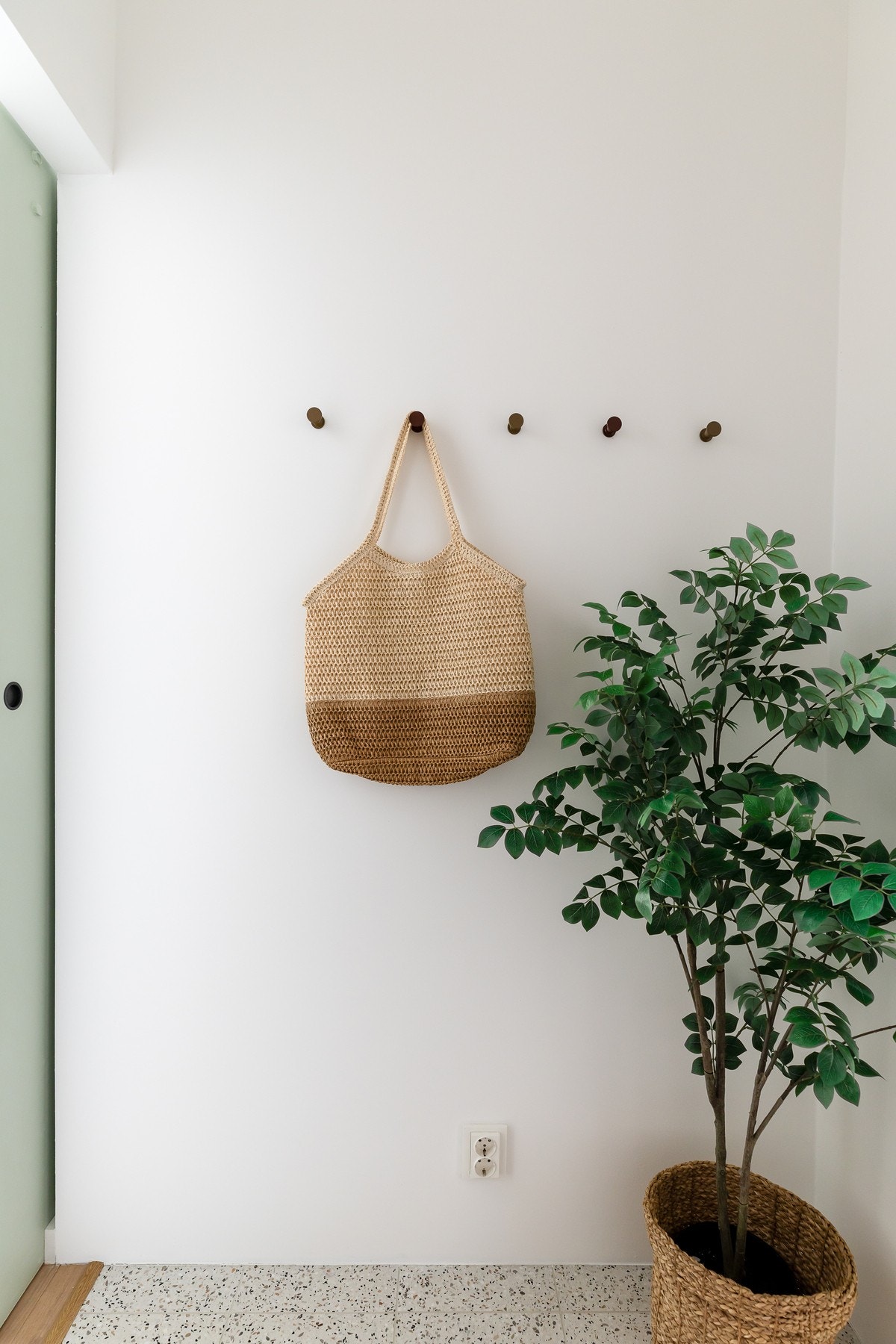 Hvit vegg med knagger og en grønn plante i en flettet kurv. Galleribilde
