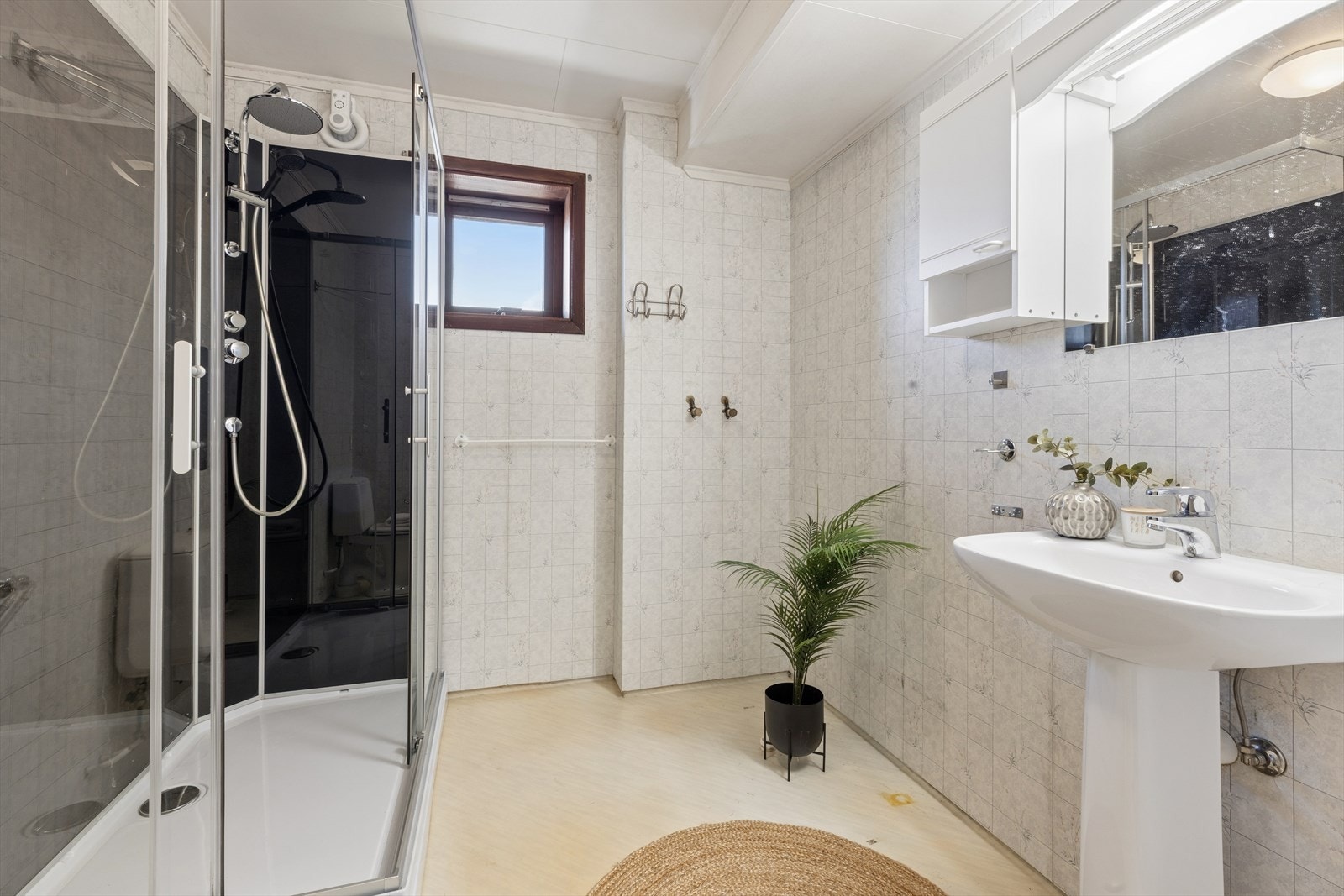 Bad med belegg på vegger og gulv med gulvvarme. Badet er innredet med servant, speil med tilhørende belysning, dusjkabinett og gulvmontert toalett. Galleribilde