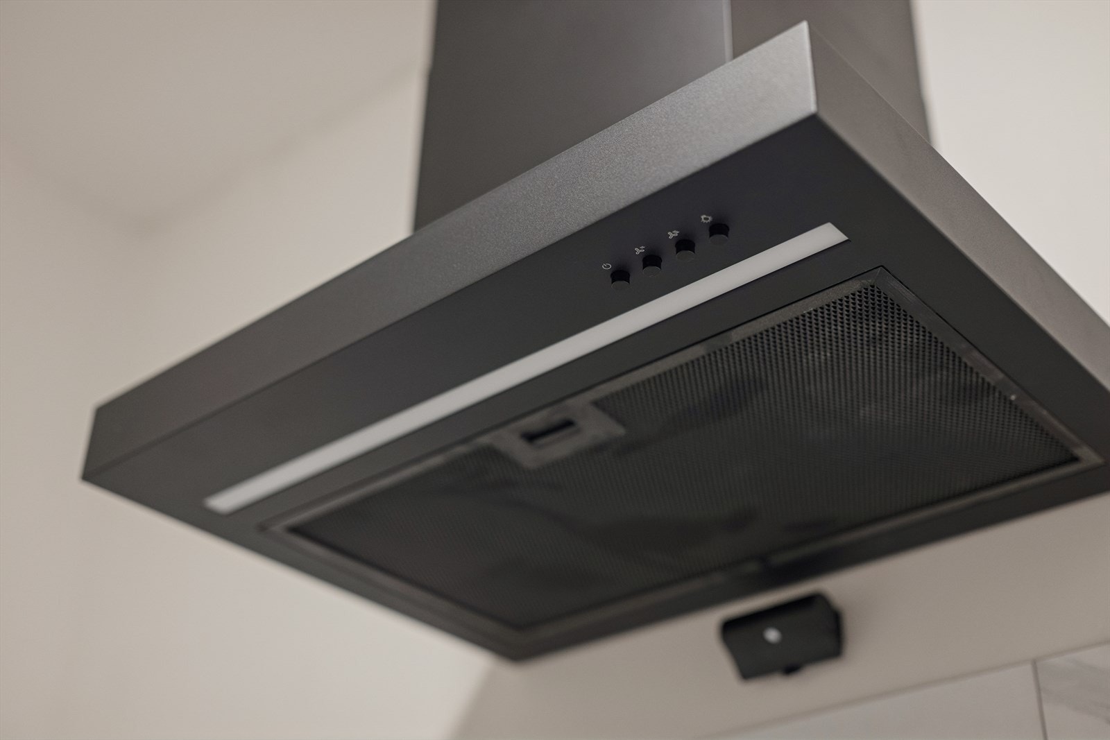 Sort kjøkkenventilator med kullfilter er plassert over kokesonen. Galleribilde
