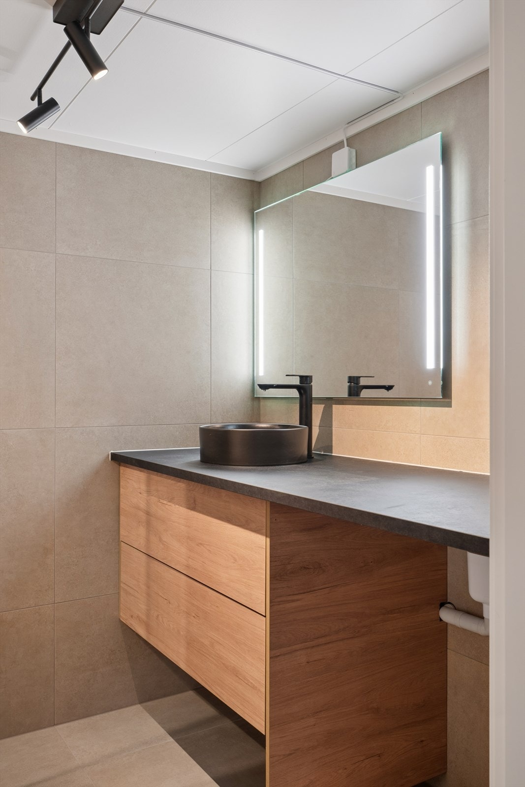 Innredningen har en heldekkende benkeplate i sort laminat og speil med integrert LED-belysning. Galleribilde