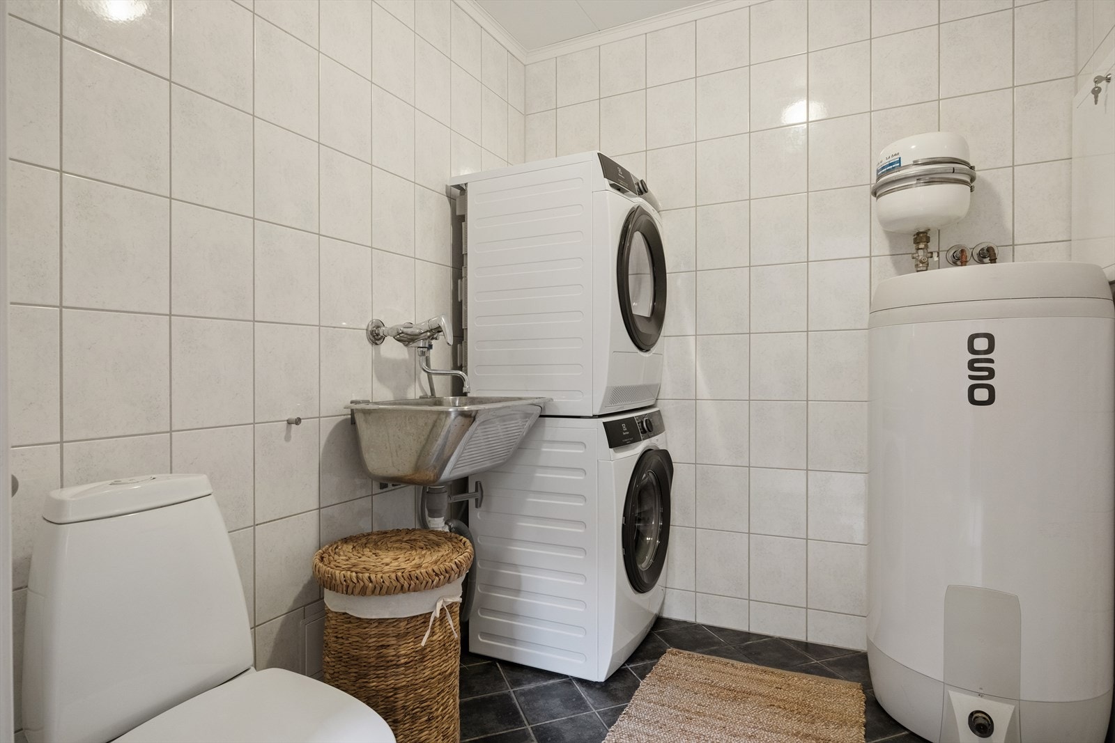 Separat vaskerom med fliser, toalett og opplegg for vaskemaskin. Varmtvannsberederen er fra 2023. Galleribilde