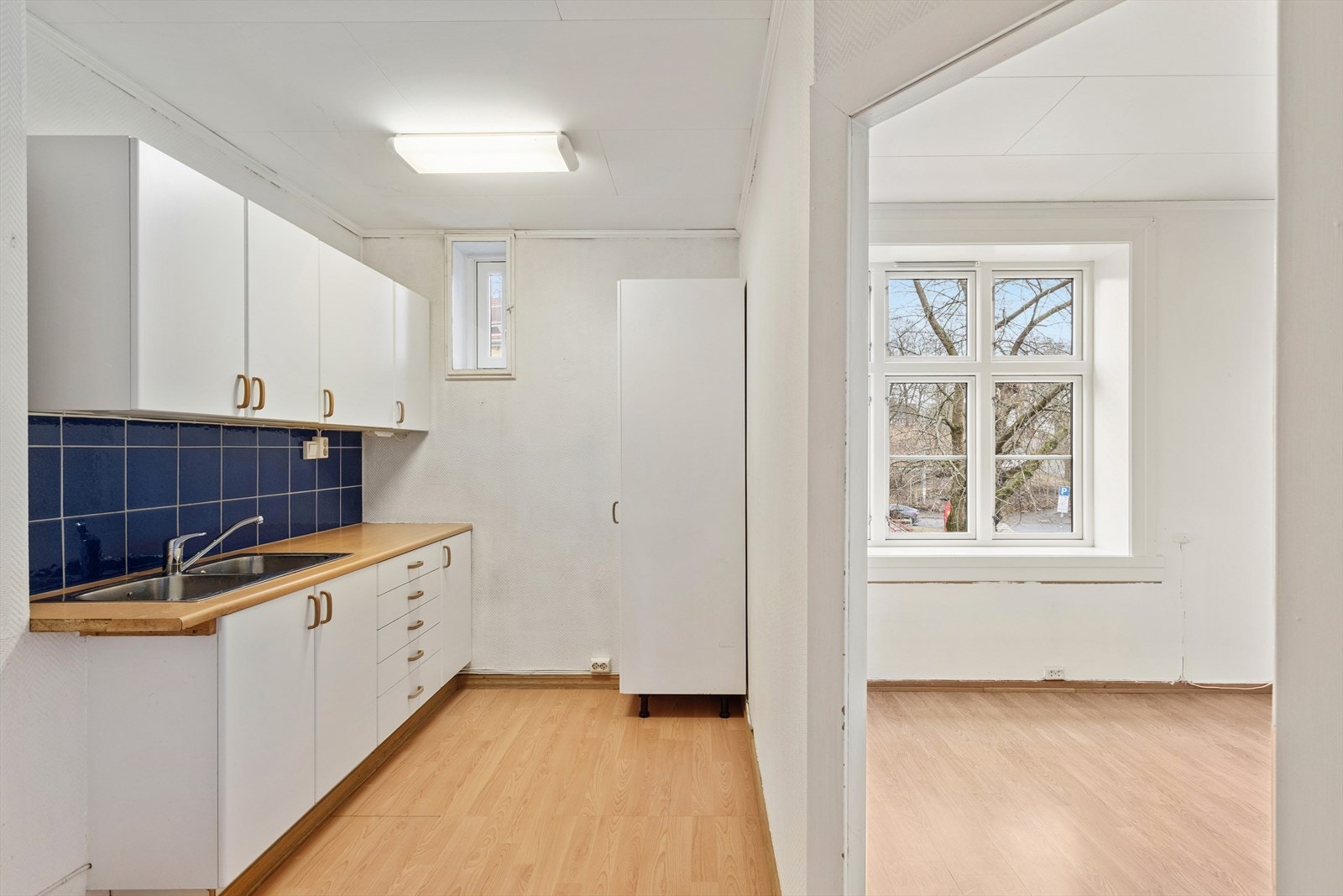 Eldre kjøkkeninnredning med glatte fronter og laminat benkeplate med nedfelt dobbel oppvaskkum. En 28 liters varmtvannsbereder fra 2017 er integrert i benken. Galleribilde