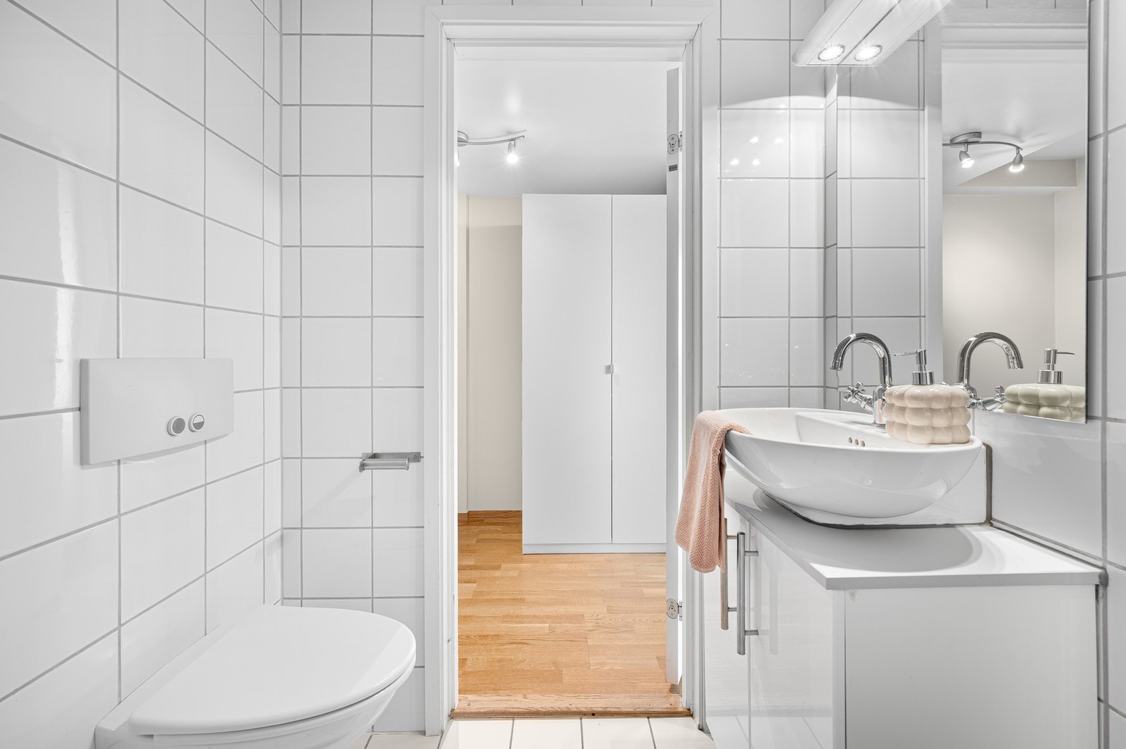 Baderomsinnredning med dusjhjørne, veggmontert wc, kran og avløp for vaskemaskin og servant med underskap og speil. Galleribilde