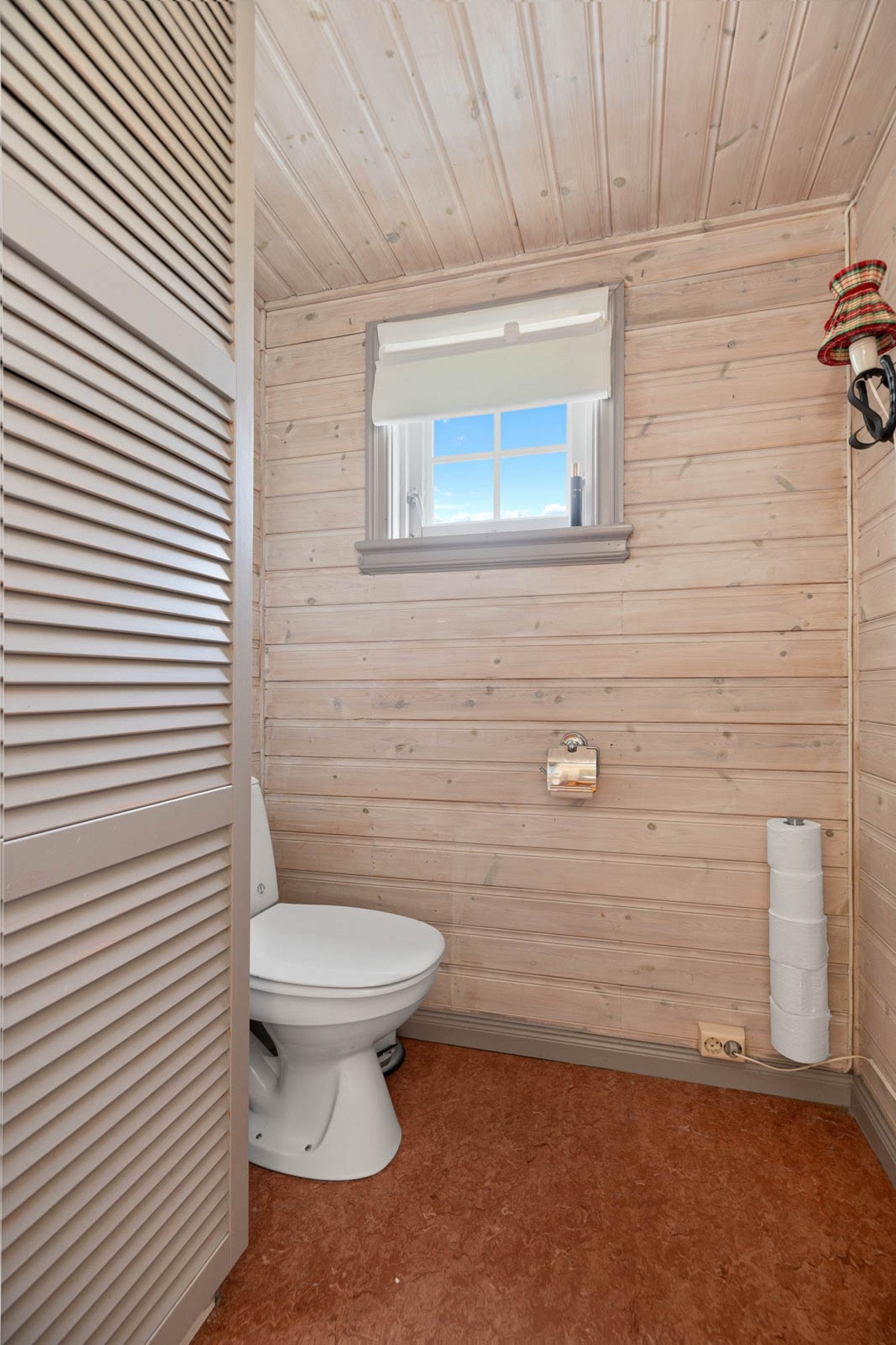 Toalettrom med vindu og panel på vegger og tak. Galleribilde
