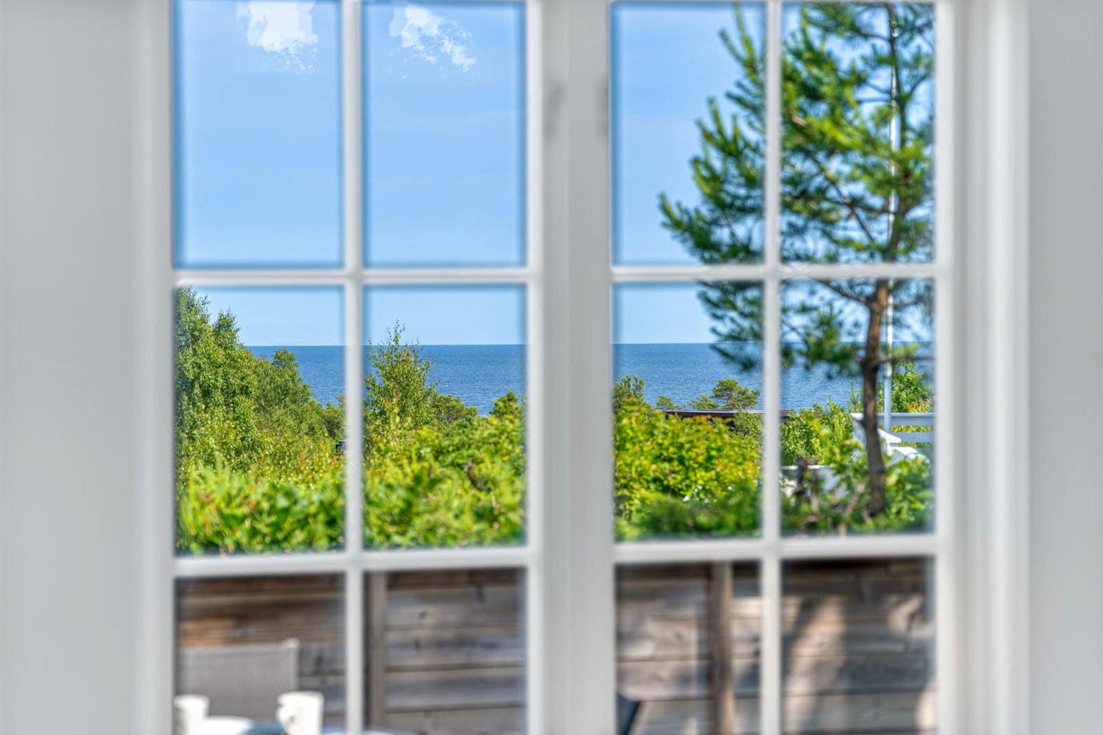 Store vinduer med utsikt mot havet og frodig vegetasjon. Galleribilde