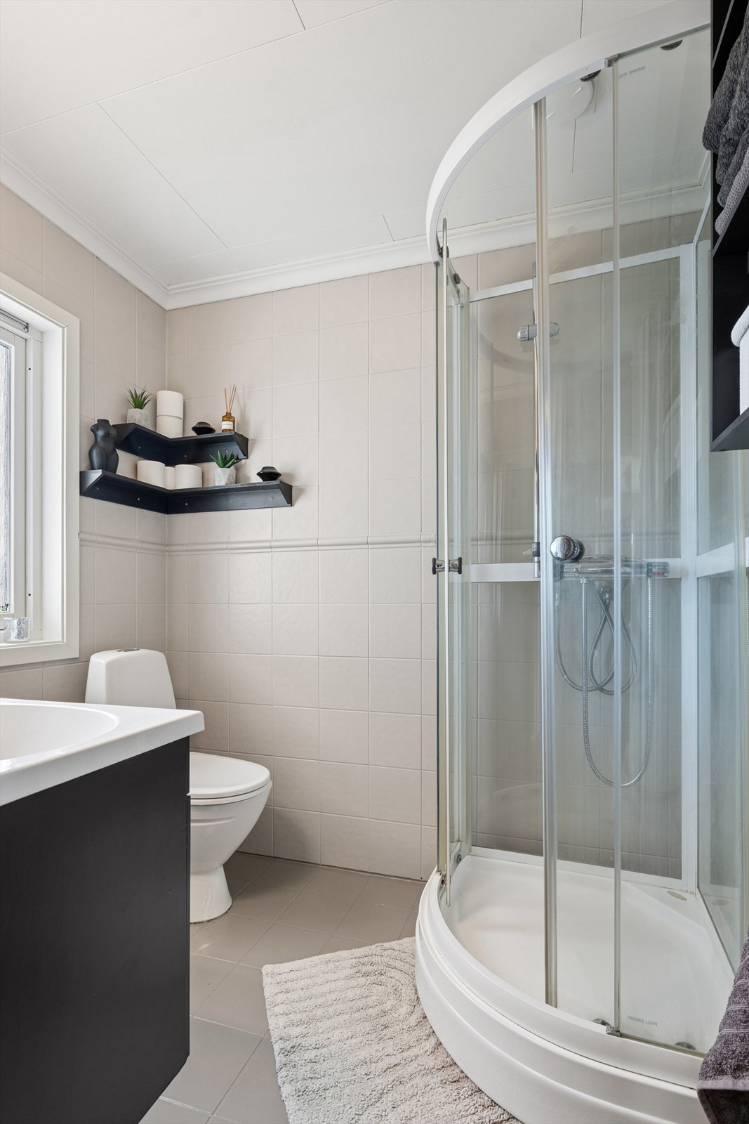 Badet med fliser på gulvene og veggene, disse er malt. På gulvet er det varmekabler. Badet er utstyrt med toalett, servant og dusjkabinett Galleribilde