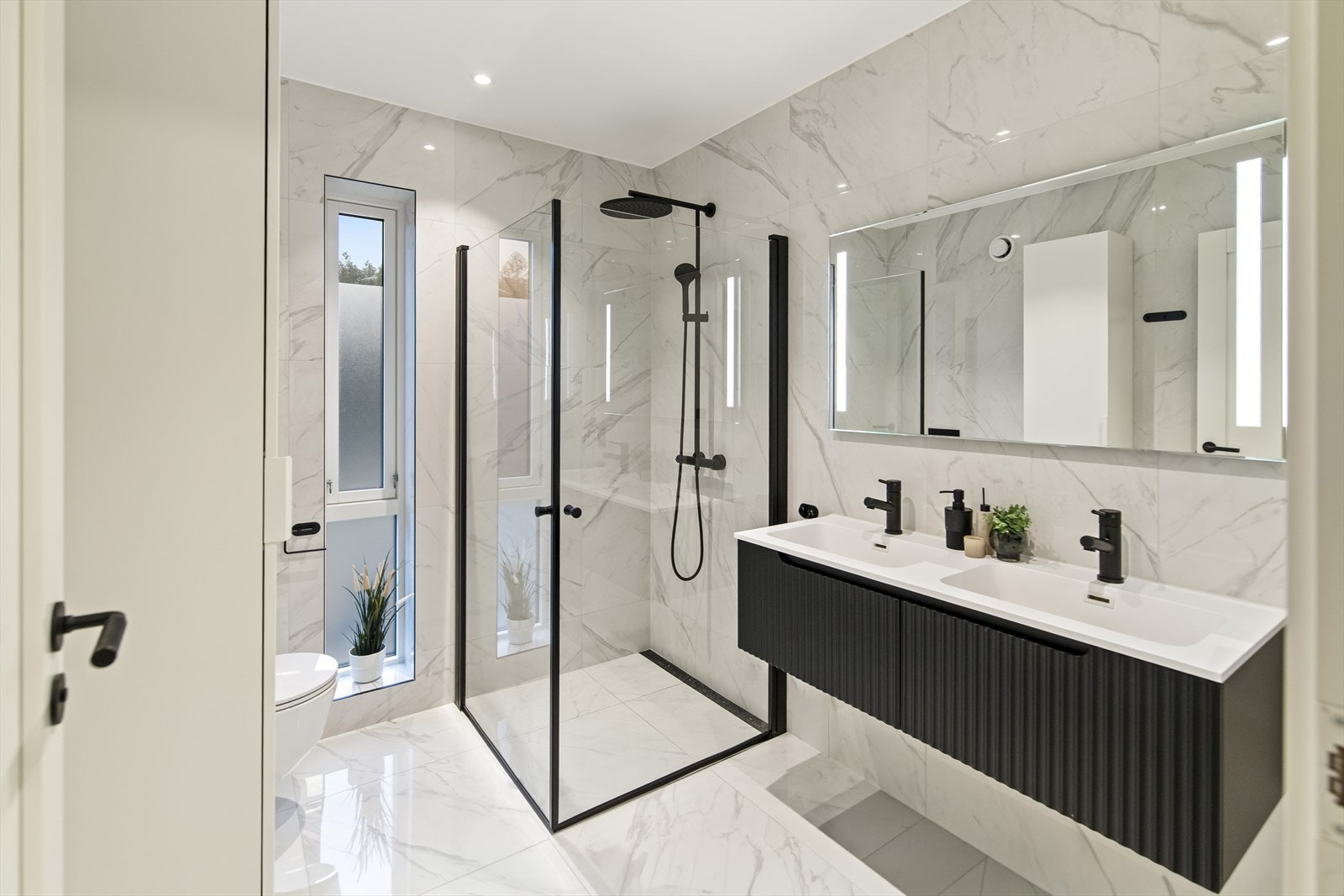 Badet er gjennomført med fliser, doble servanter, vegghengt toalett og dusj. Galleribilde