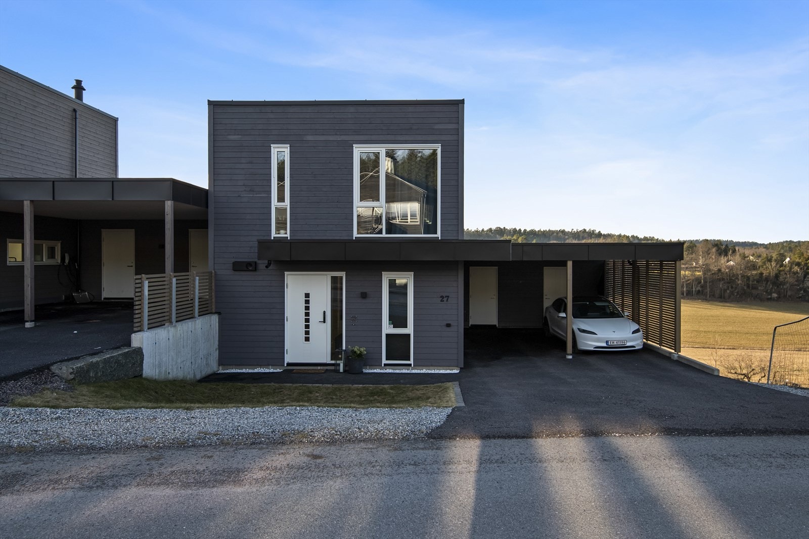 Eiendommen er moderne opparbeidet med en asfaltert gårdsplass som leder rett inn til en praktisk dobbel carport med elbillader. Galleribilde