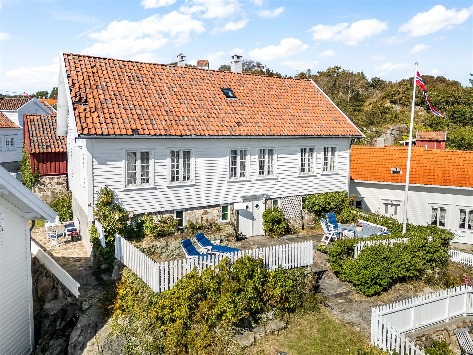 Idyllisk beliggende feriebolig med nydelig uteplass omgitt av hvitmalt stakittgjerde. Taksteinen ble lagt tilbake rett etter bilde ble tatt. Galleribilde