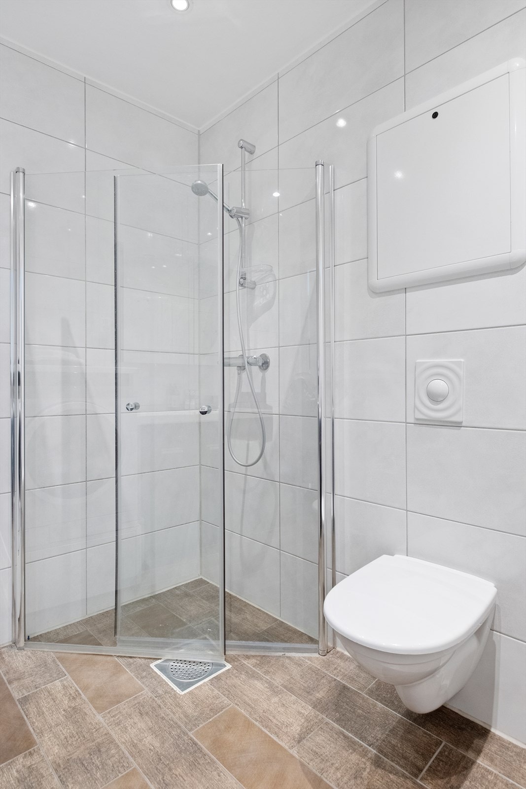 Badet er utstyrt med heldekket servant, speilskap, veggmontert toalett, dusjvegger/hjørne og opplegg for vaskemaskin Galleribilde