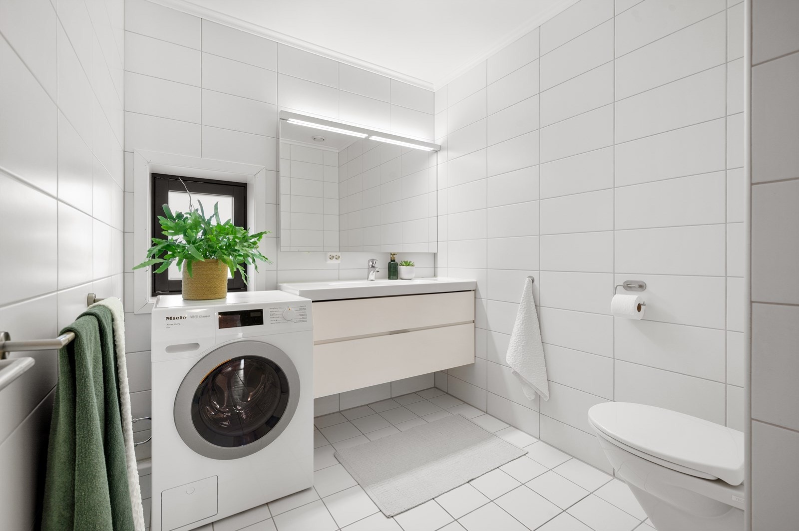 Moderne flislagt baderom med varme i gulv. Innredning med servant, vegghengt klosett, opplegg for vaskemaskin, dusjnisje og mekanisk avtrekk. Galleribilde