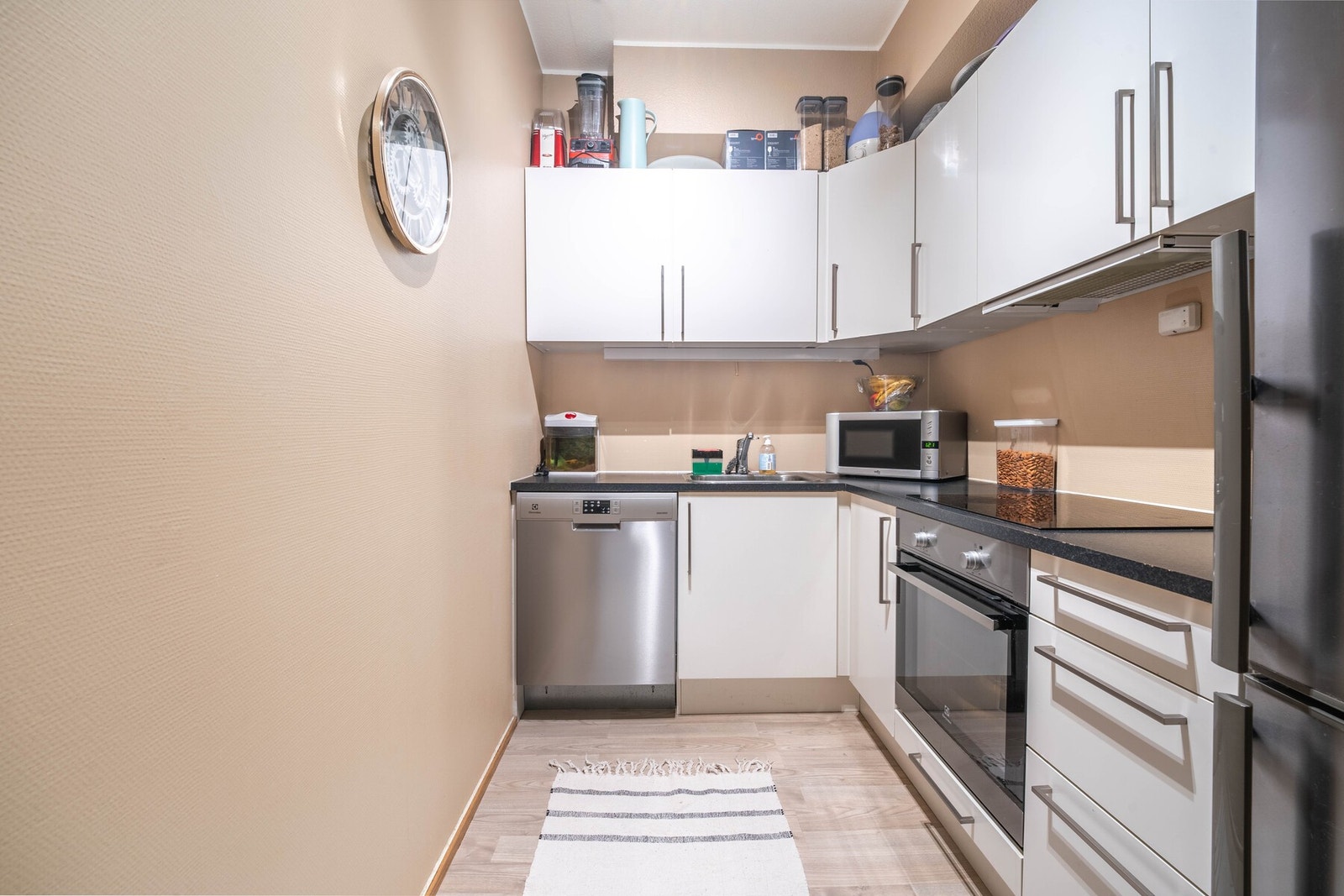 Kjøkkeninnredning med glatte fronter og benkeplate med laminert overflate samt nedfelt oppvaskkum med ett-greps armatur, benkeskapsbelysning og stikkontakter under overskap Galleribilde