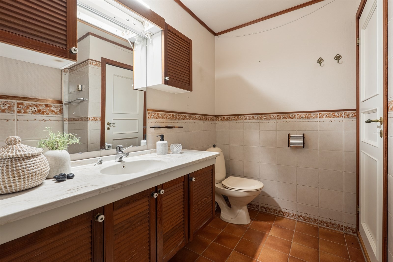 Badet har eldre utførelse med flislagte overflater og varmekabler i gulvet. Rommet er utstyrt med klosett, heldekkende servant med over- og underskap, samt badekar. Galleribilde